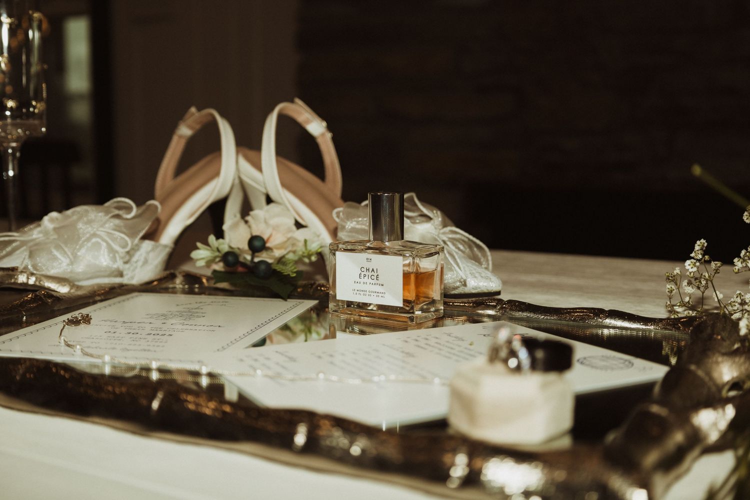 Wedding details including white heels, perfume bottle, and invitation on elegant table setting.
