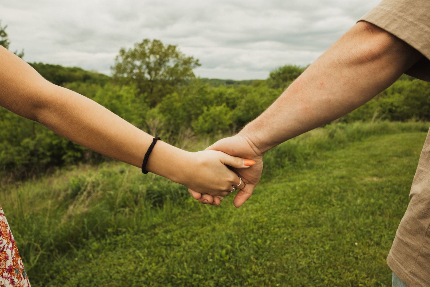 Two people holding hands in a scenic green meadow on an overcast day.