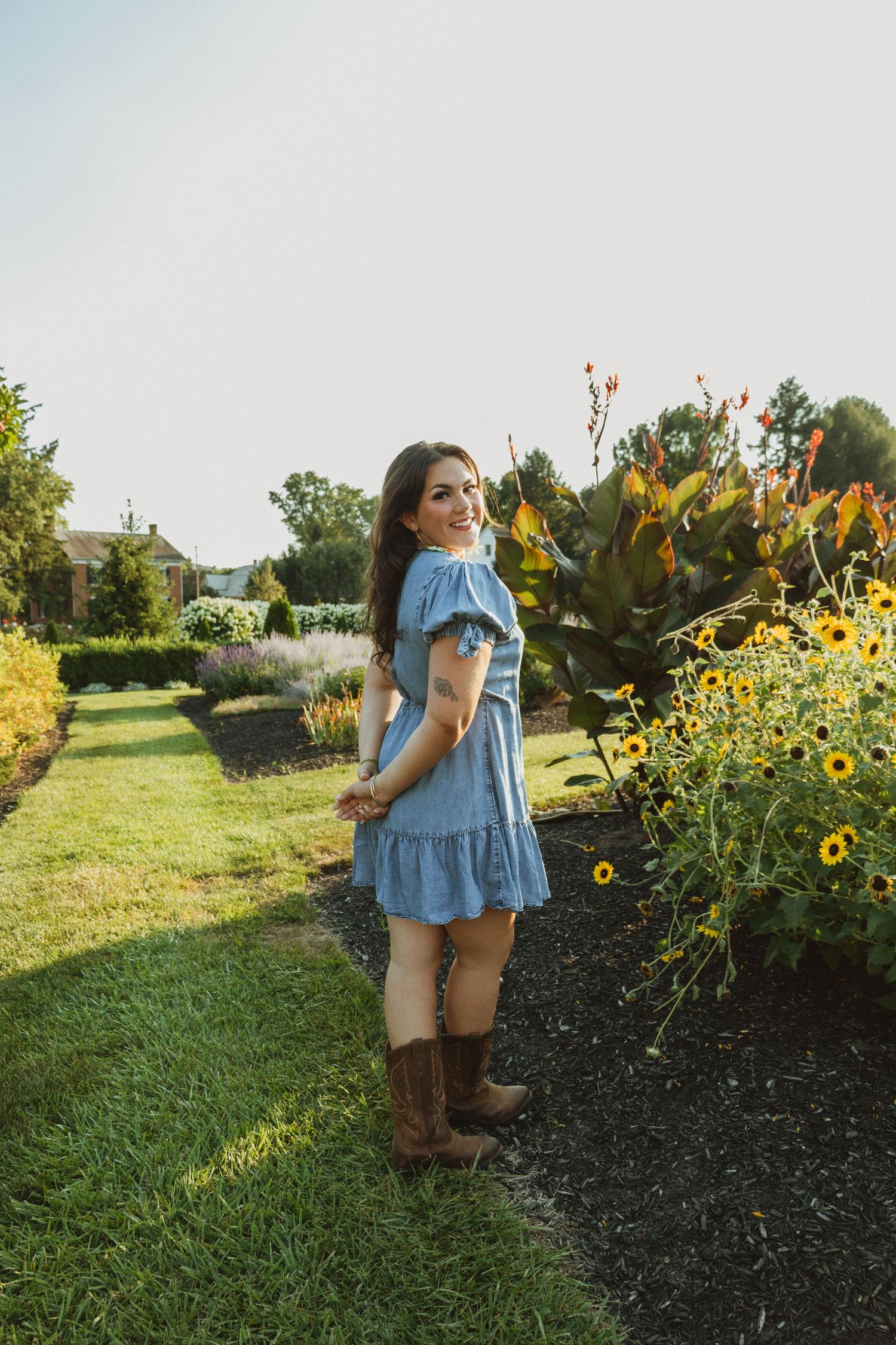 A light blue dress and brown boots complement a sunny garden setting with blooming sunflowers on a summer day.