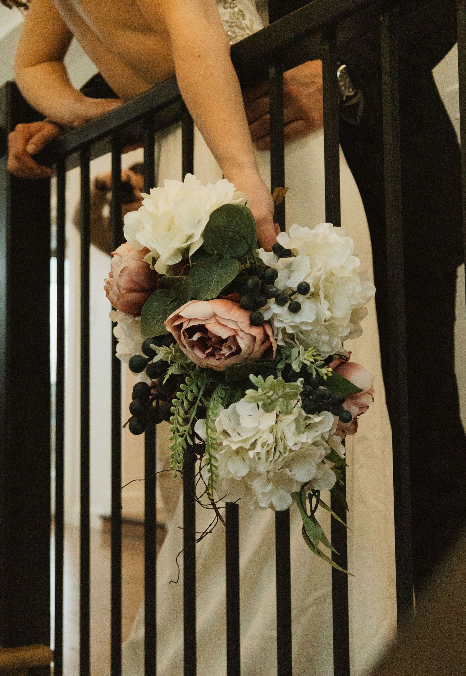 Elegant wedding bouquet with white hydrangeas and pink roses held against black railing.
