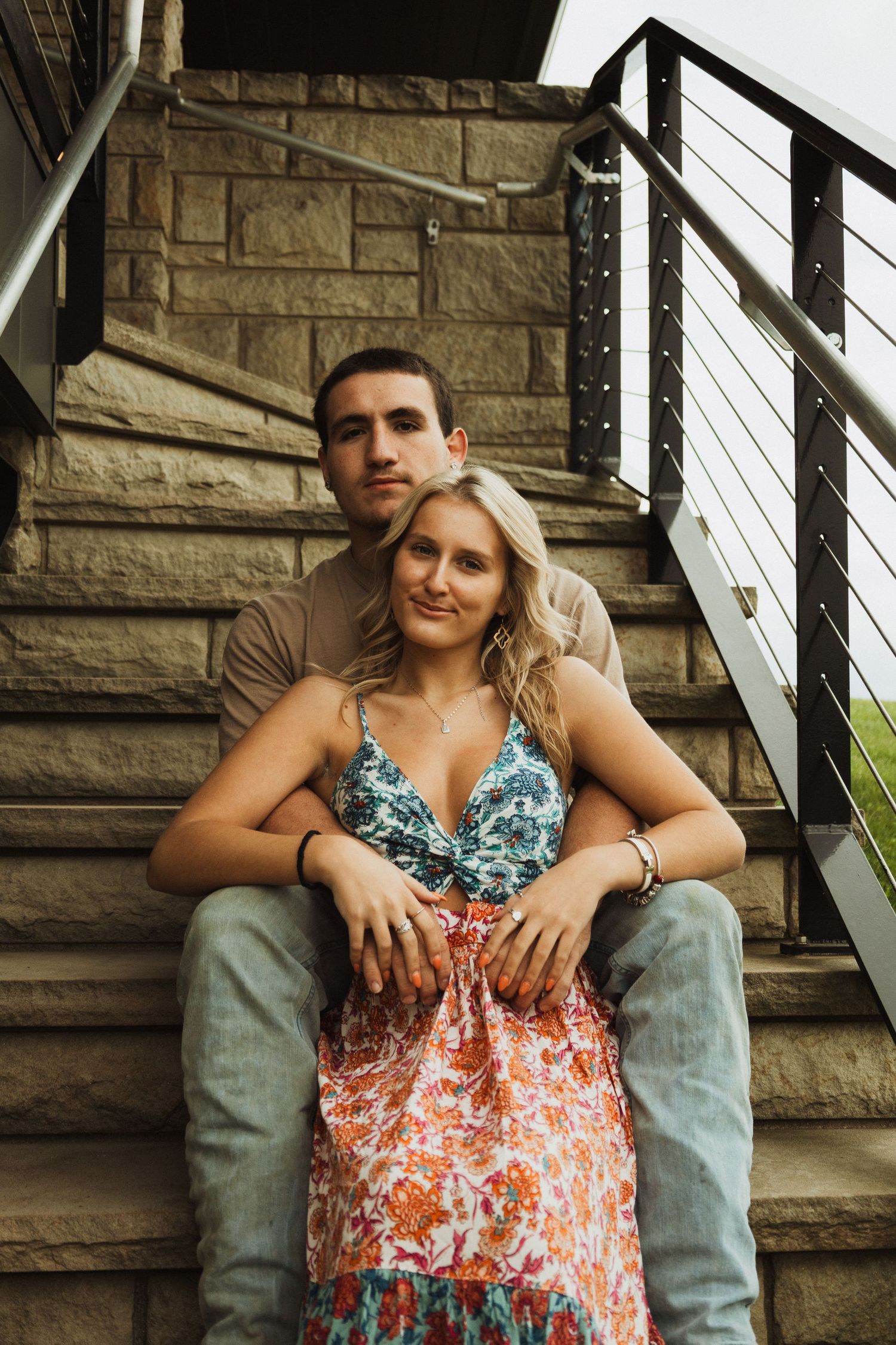 A couple poses on stone steps with modern metal railings.