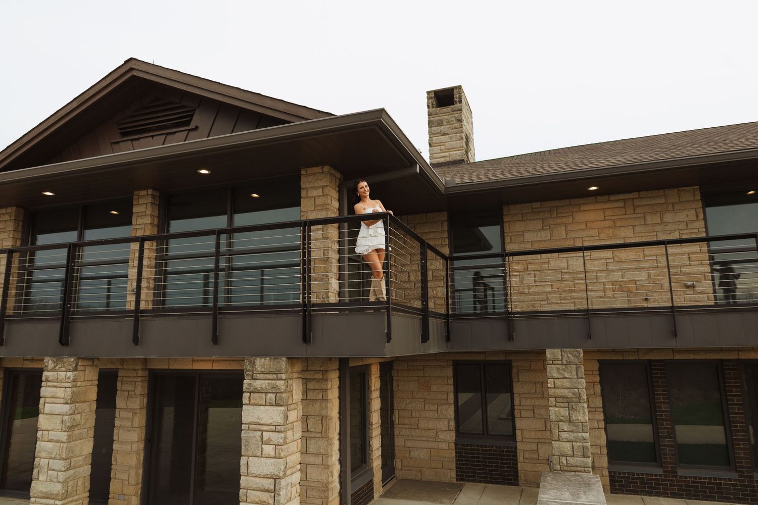 Woman standing on a balcony of a modern stone and brick luxury home with large windows.