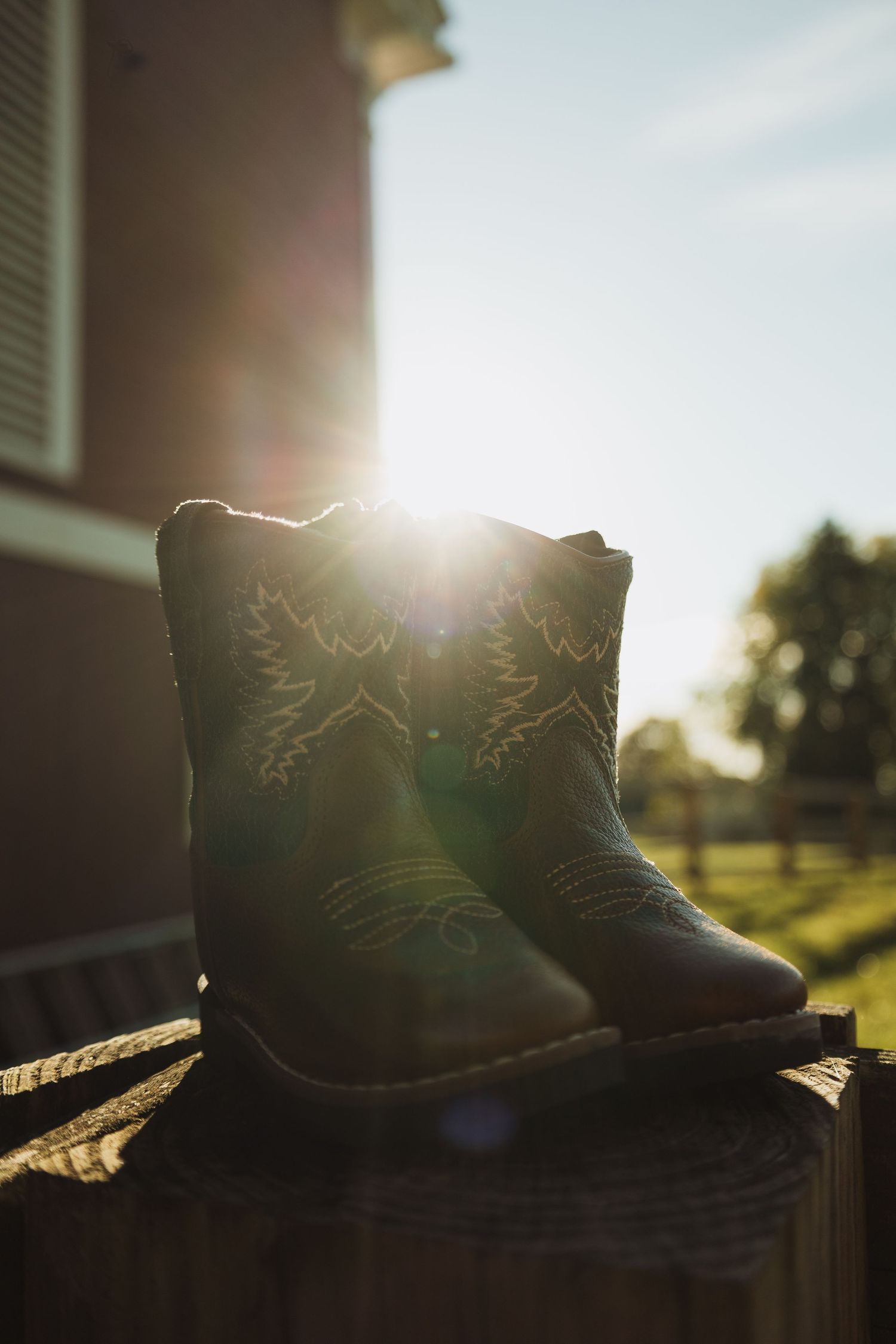 Black cowboy boots silhouetted against sunlight with lens flare creating a warm golden glow at sunset.