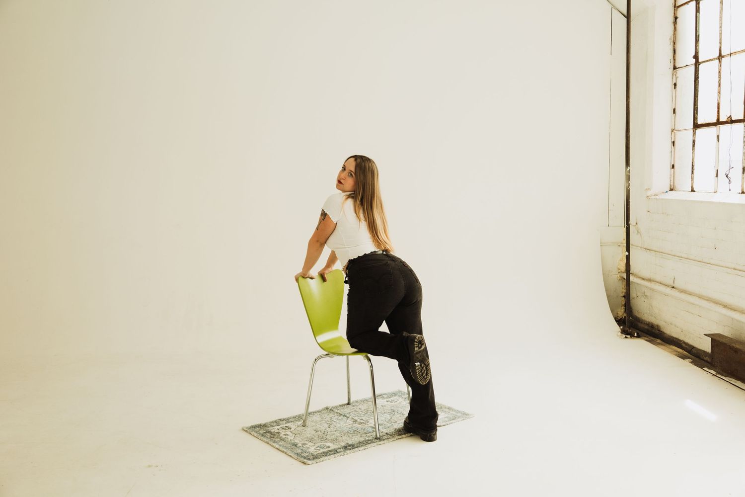 Person sitting backwards on green chair in minimalist white studio space.