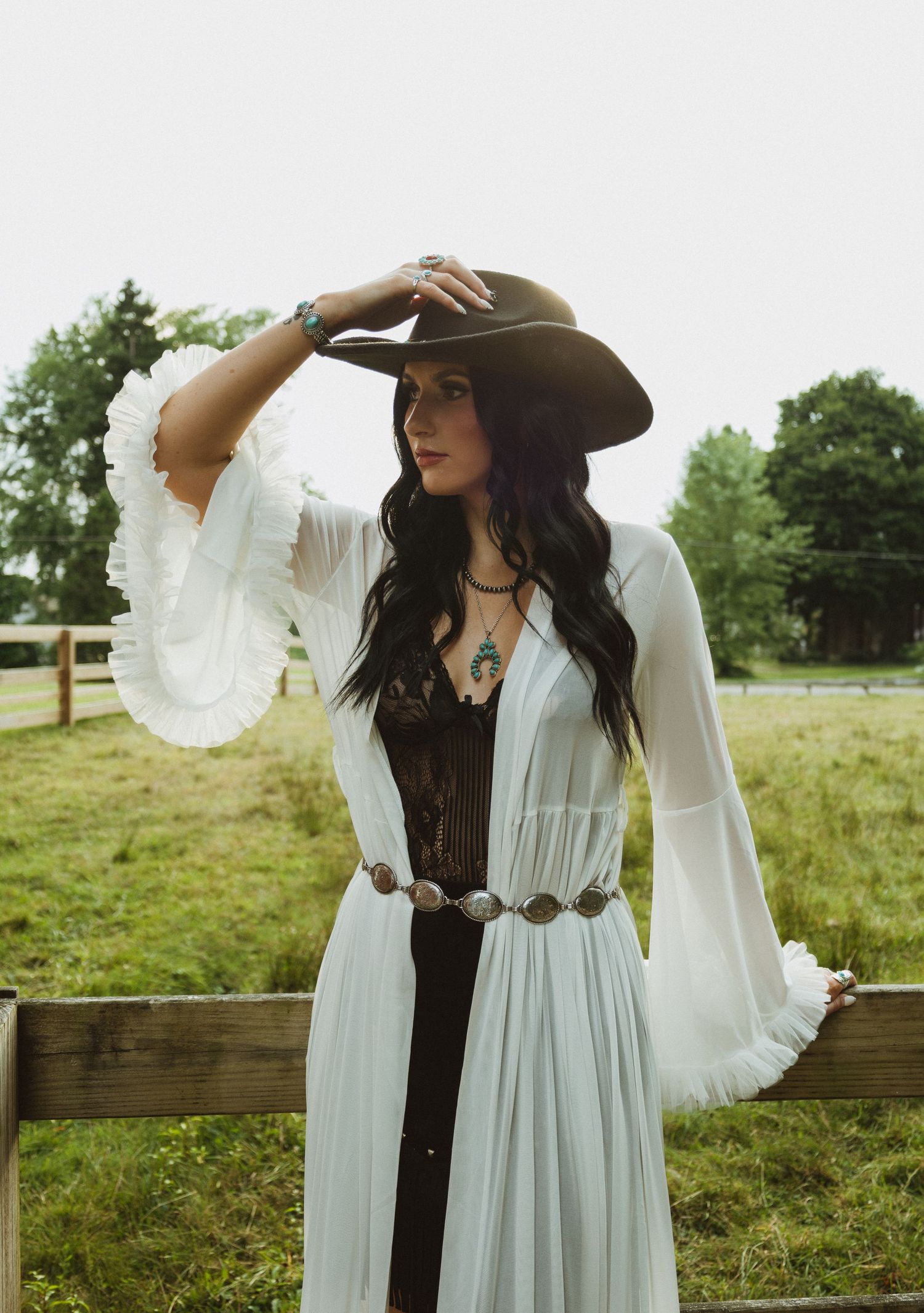 A flowing white dress with bell sleeves pairs with a dark western hat for a bohemian ranch photo.
