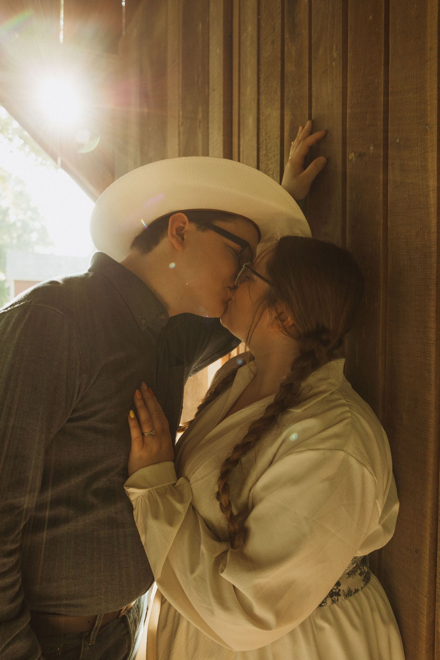 A romantic couple in cowboy attire share intimate moments in front of a rustic wood paneled background.