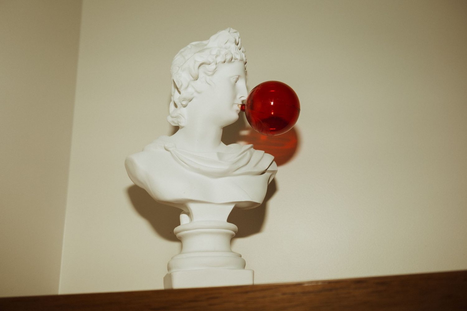Classical white bust sculpture with a red apple displayed on a shelf.