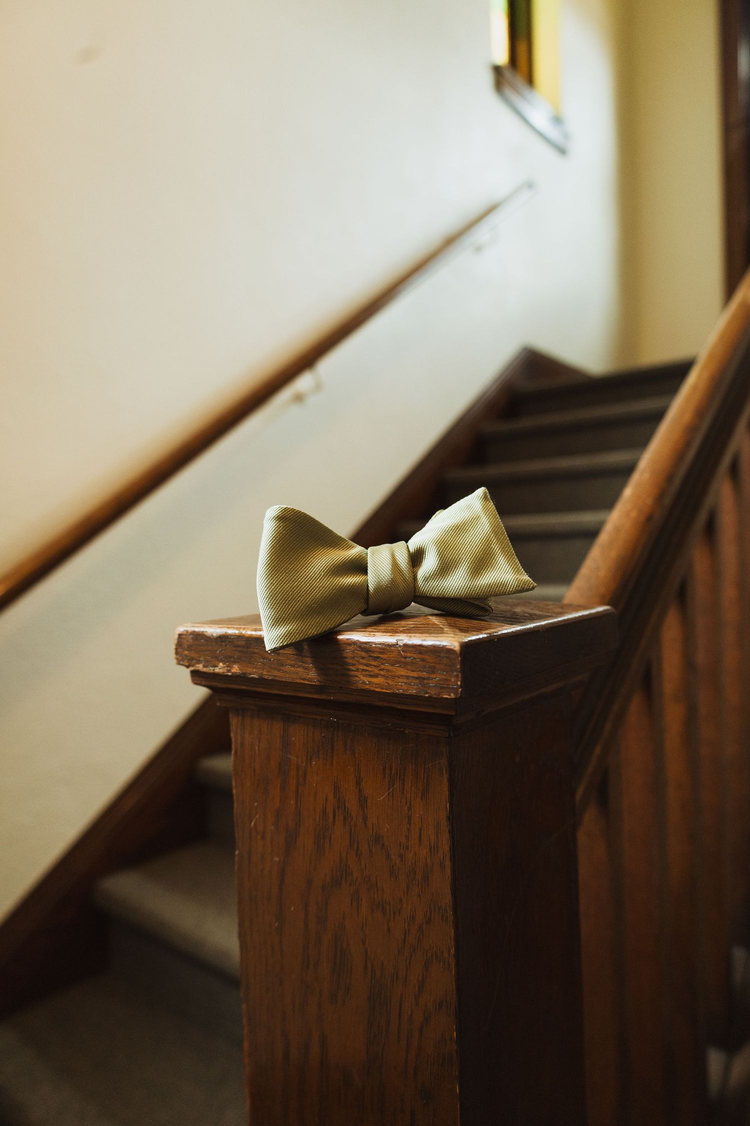Sage green bow tie resting on dark wooden staircase banister in vintage venue.