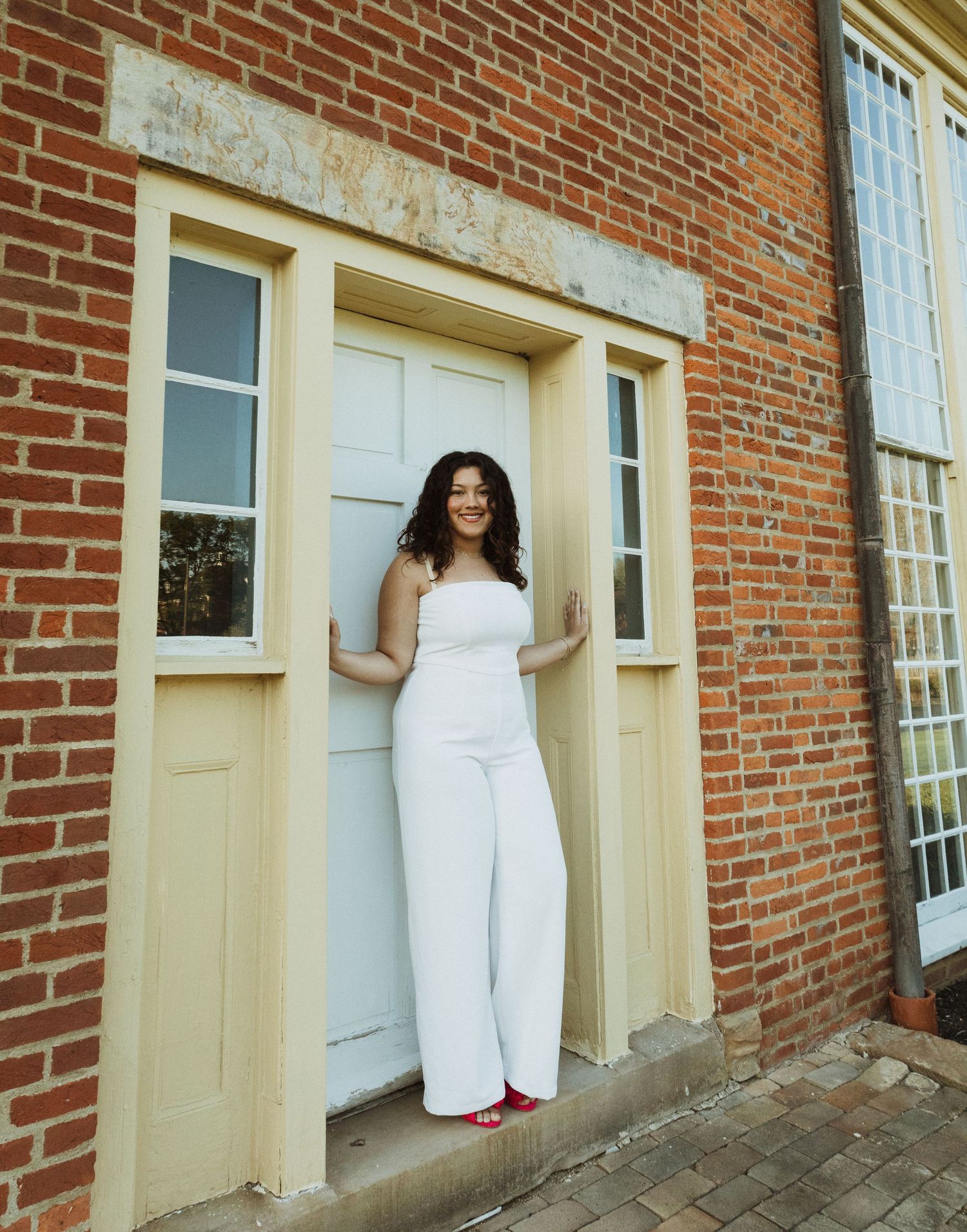 A woman in an all-white outfit stands confidently against a vintage doorway.