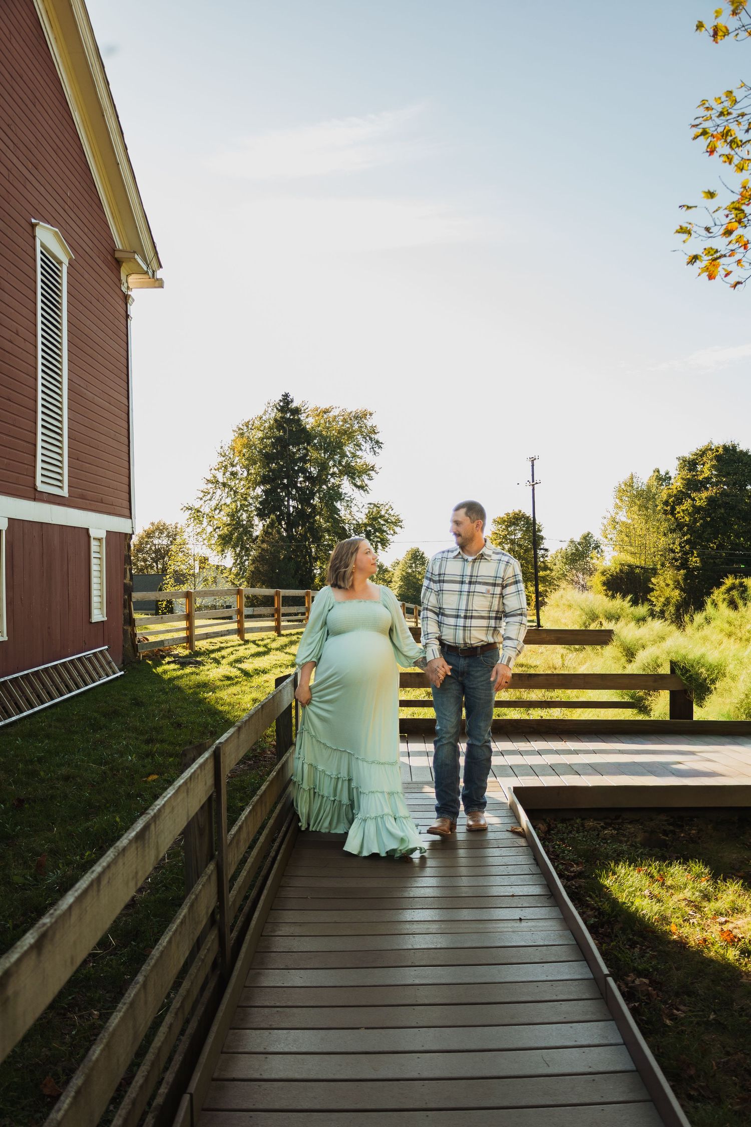 A couple walks together on a wooden deck outside a brown house during a sunny afternoon.