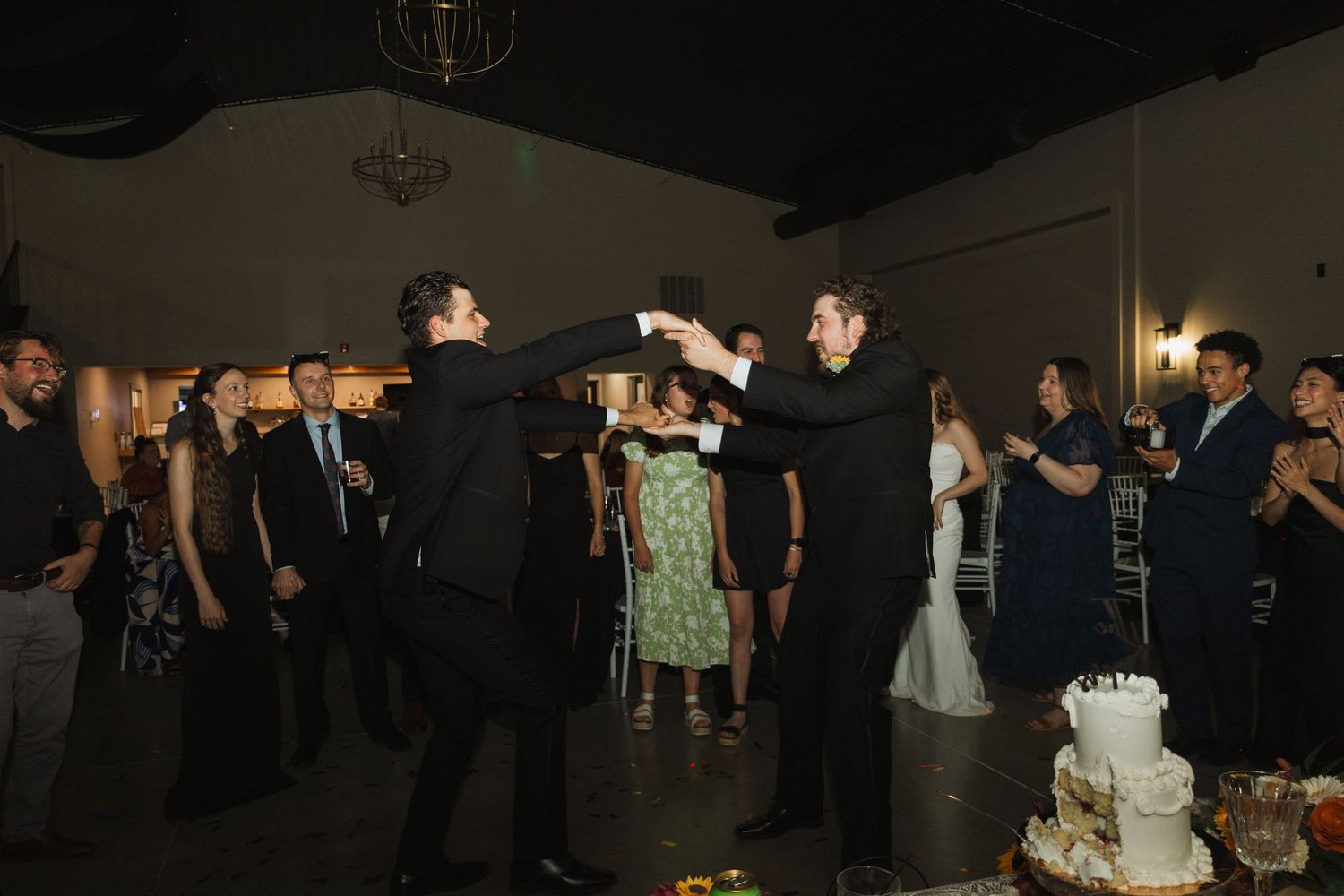 Wedding guests dance and celebrate on a dimly lit dance floor during an evening reception.