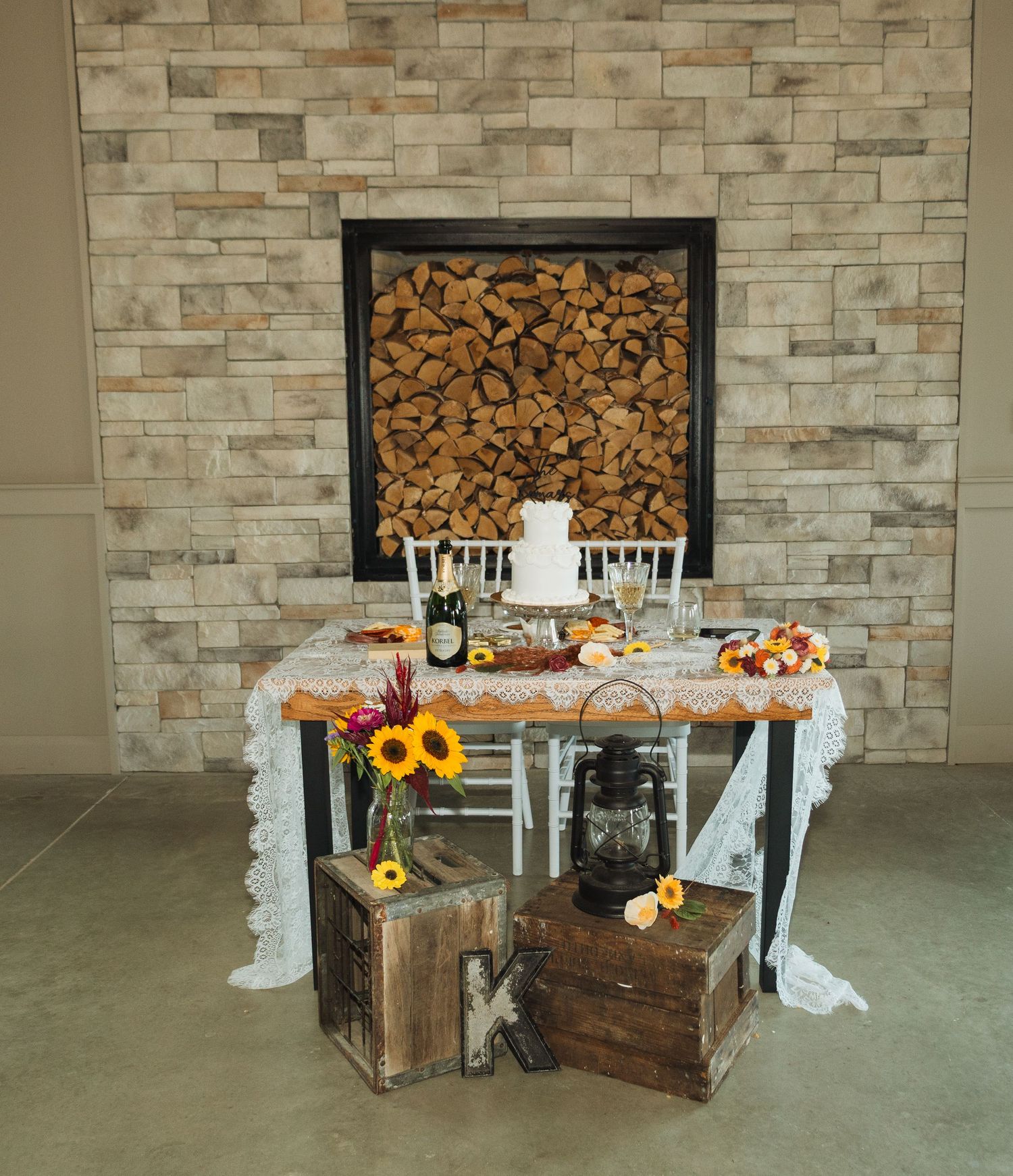 Rustic wedding decor setup with wooden crates, sunflowers and white fabric against a stone wall.