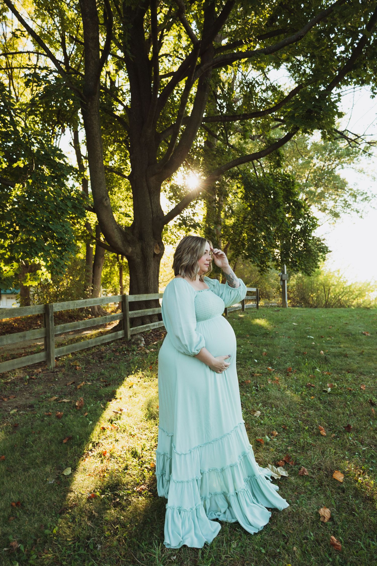 Couple in matching mint green dresses embrace in a sunlit park setting with wooden fence and autumn leaves.