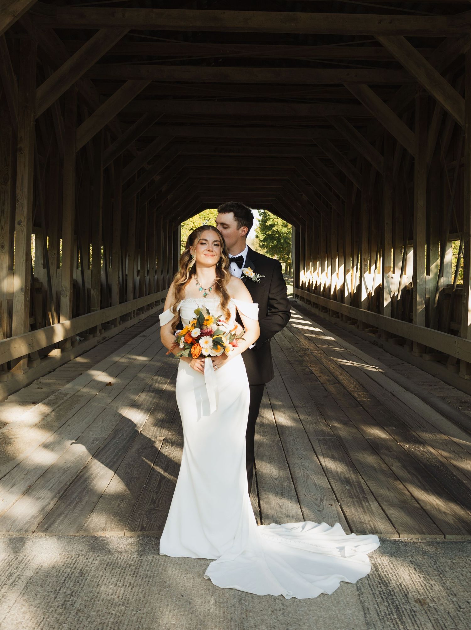 Sunlit covered wooden bridge creates dramatic shadows for wedding portraits.