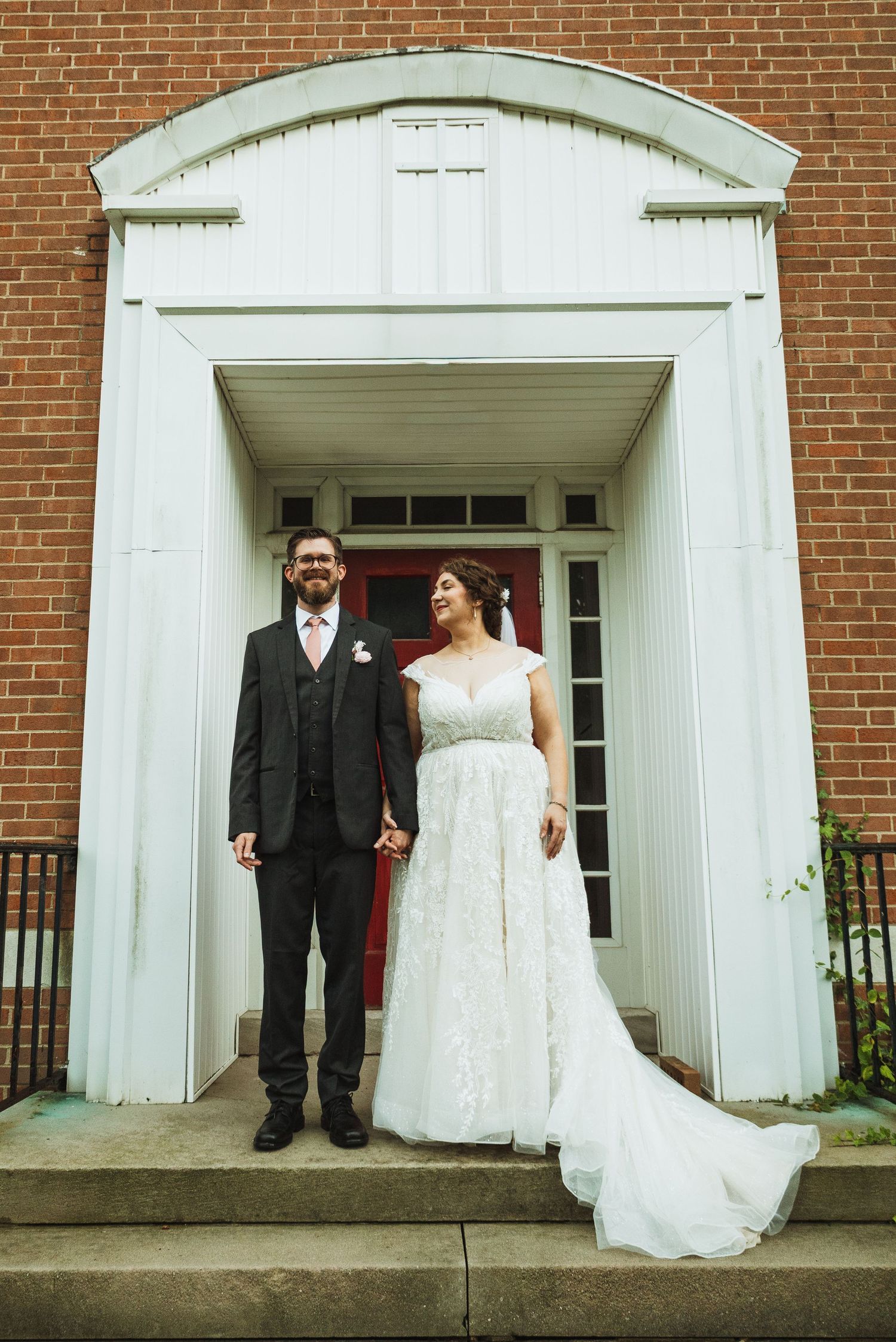 A bride and groom stand together in front of an elegant brick building entrance.
