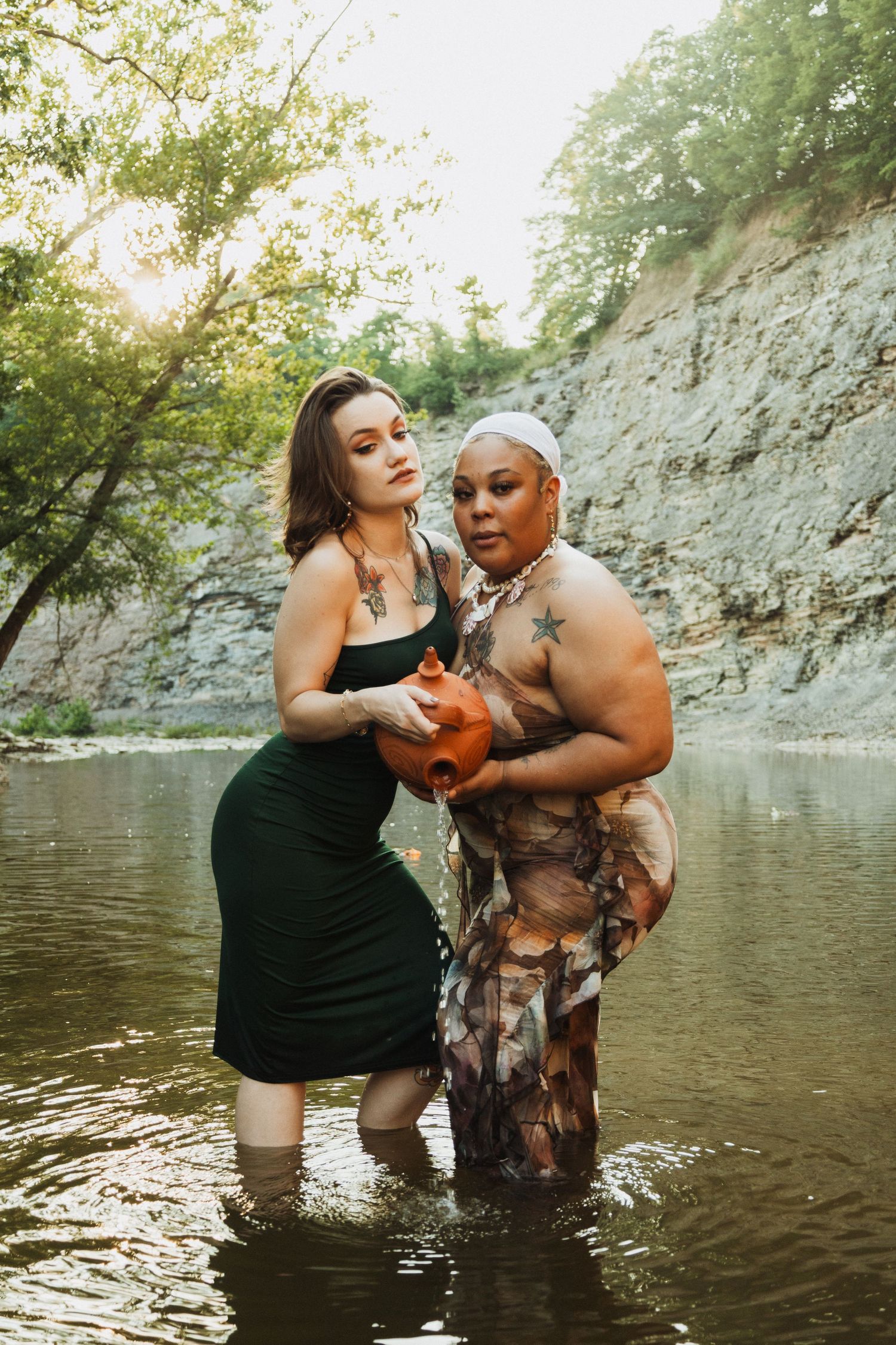 A couple shares joyful moments while wading and playing in a creek with rocky cliffs in the background during golden hour.