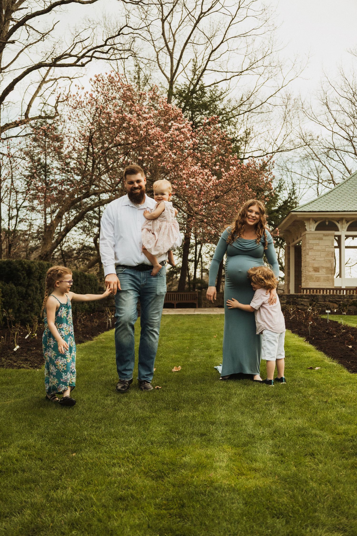 Family portrait in a garden setting with blooming cherry trees and a gazebo in the background.