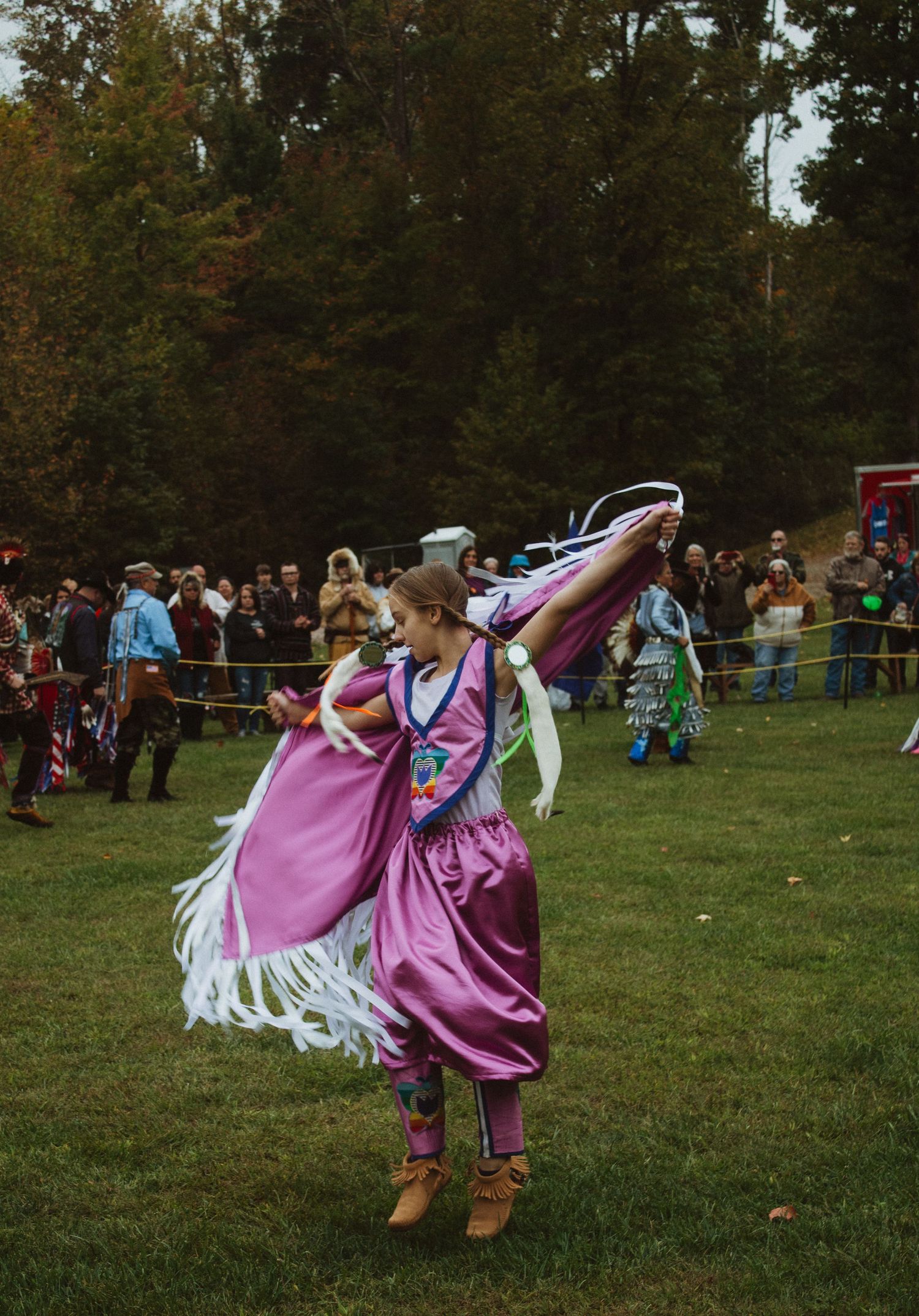 A dancer in a flowing pink and white dress performs traditional movements at an outdoor festival.