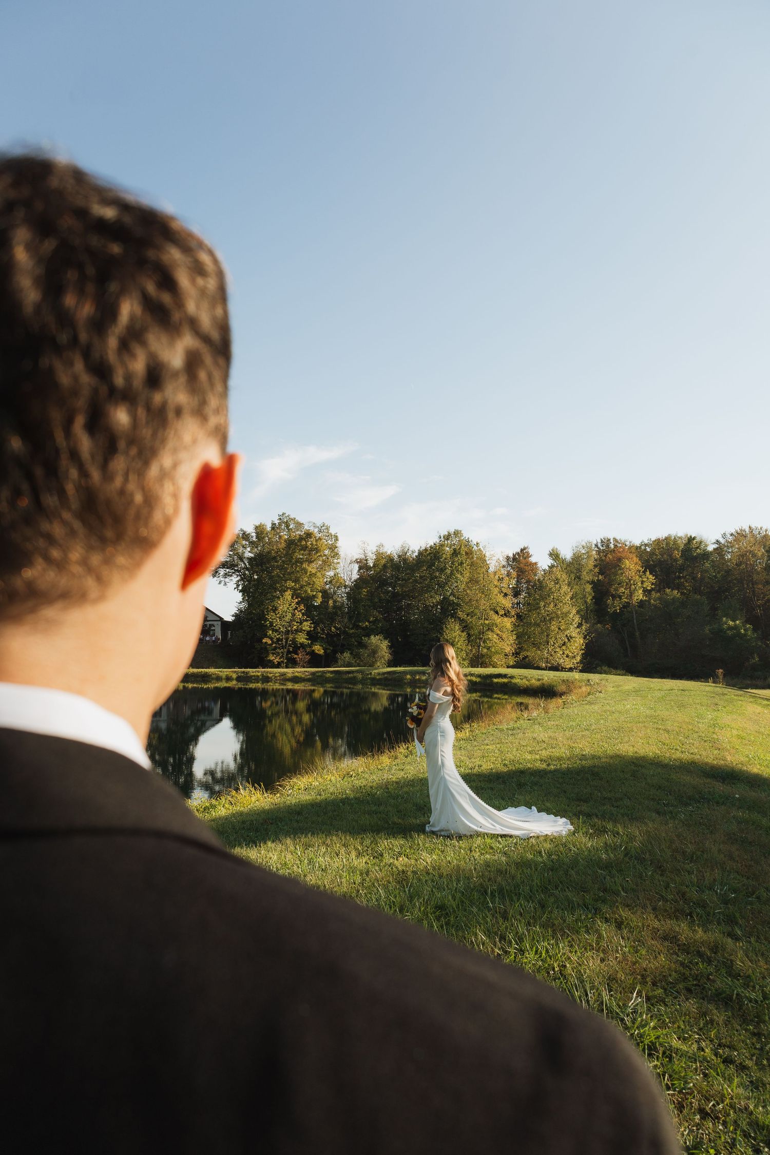 A wedding couple stands in a sunlit meadow surrounded by trees during golden hour photography.