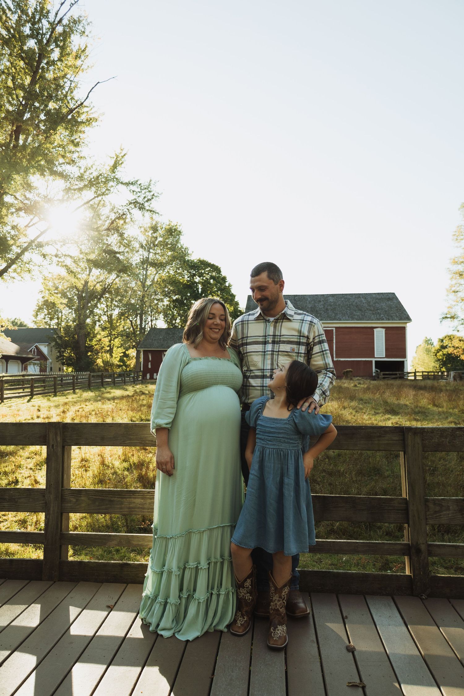 Family poses together on a wooden deck during golden hour with trees and buildings in background.