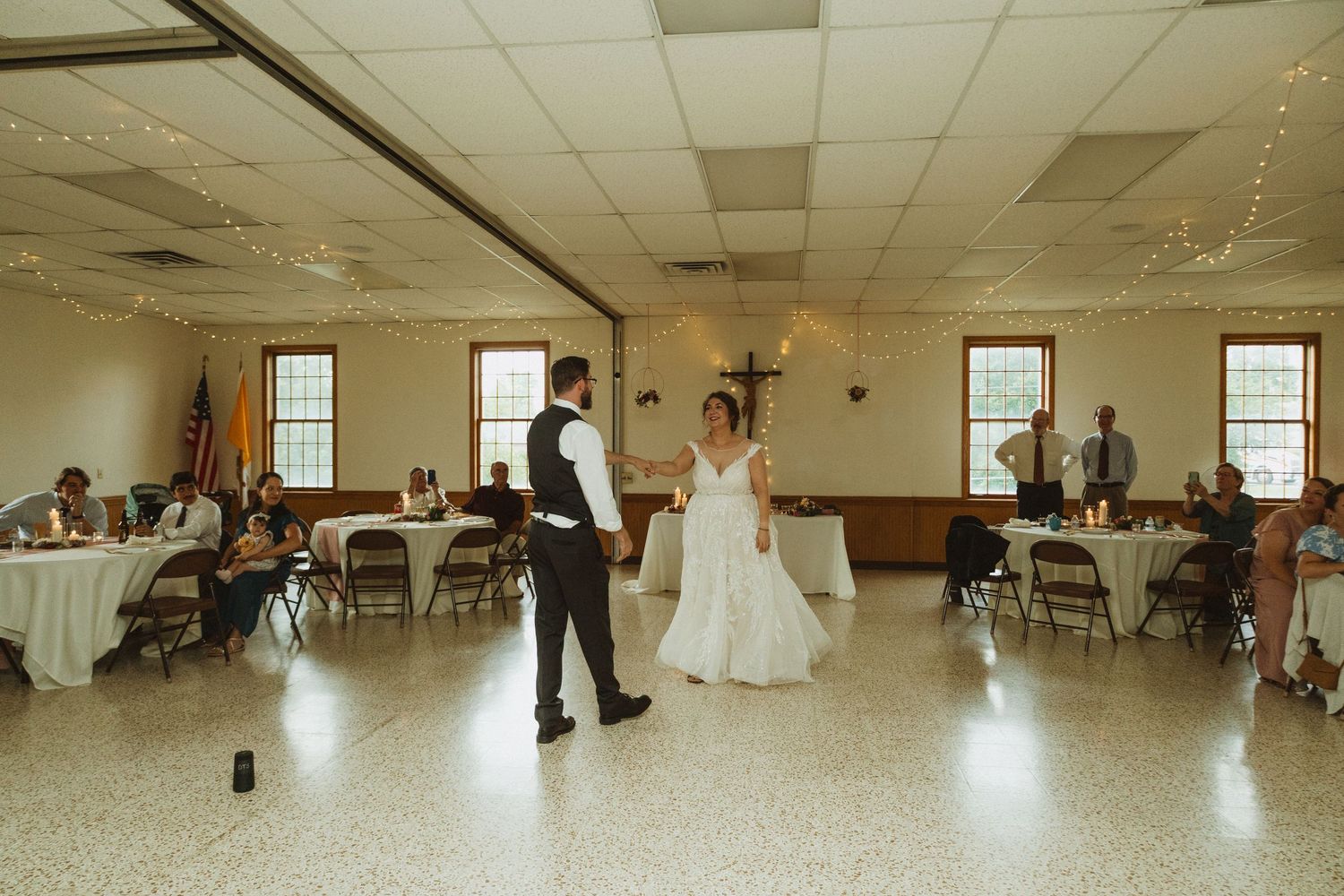 A panoramic view of a spacious reception hall with guests seated at round tables.