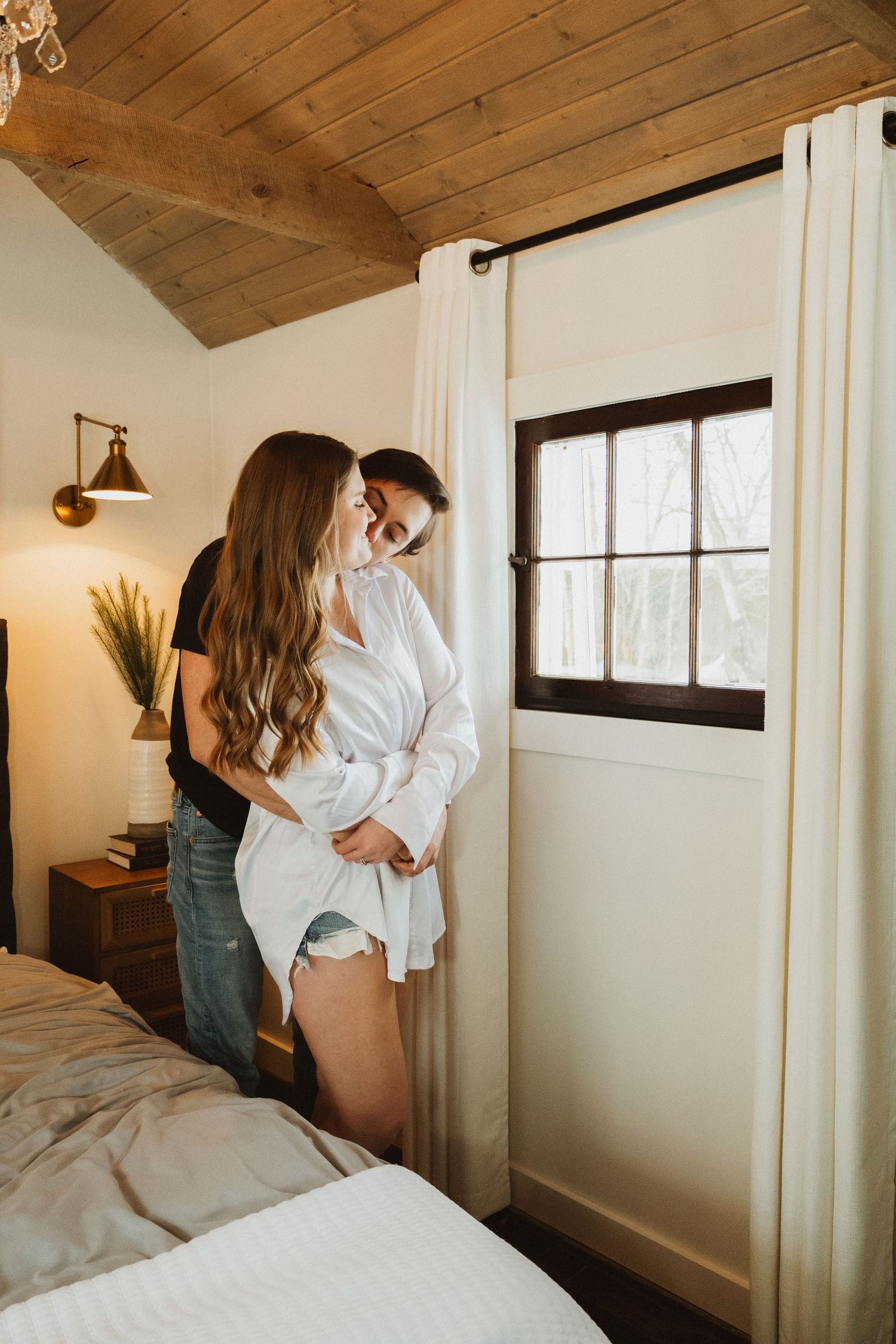 Sunlit bedroom scene with wooden ceiling, white curtains and modern wall decor.