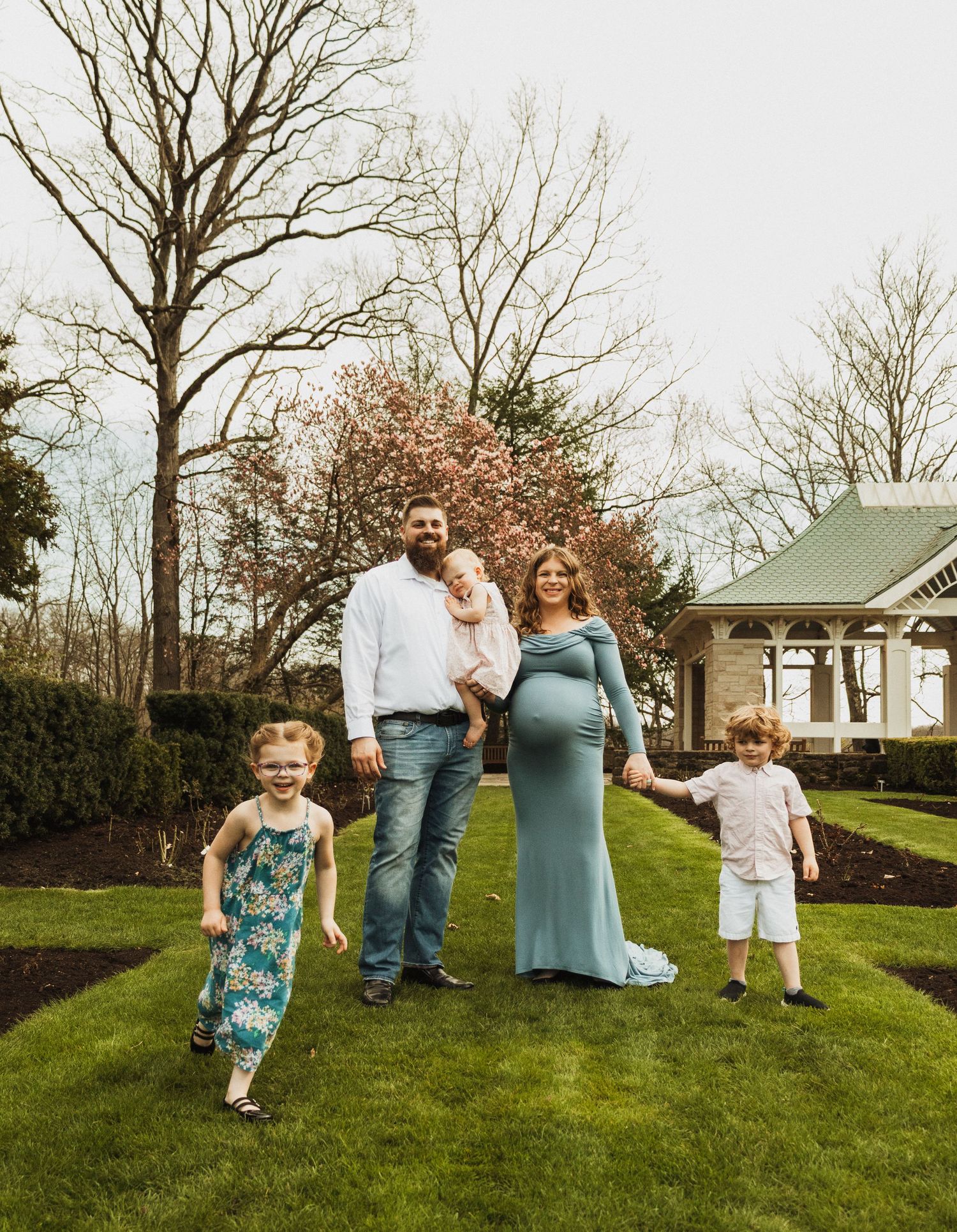 A family stands together on a spring lawn with blooming cherry trees and a house in the background.