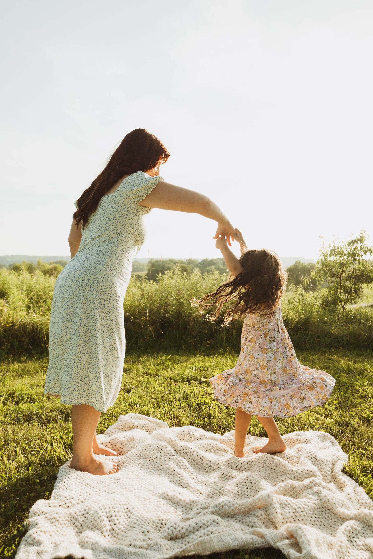 A tender moment captured between parent and child dancing on a white lace blanket in a sunny field.