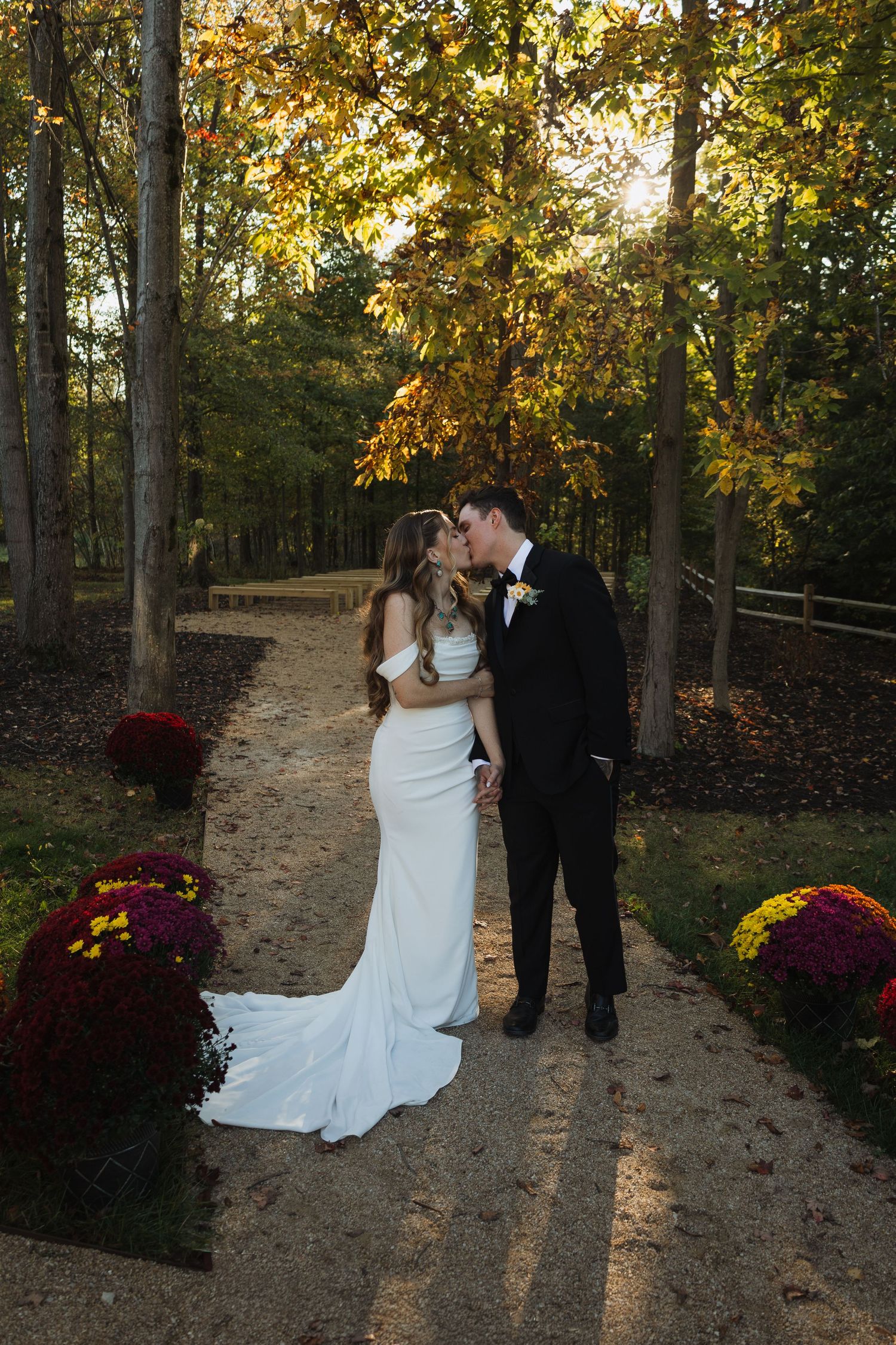 Romantic outdoor wedding photos of couple in autumn woods with colorful mums and golden sunlight filtering through trees.