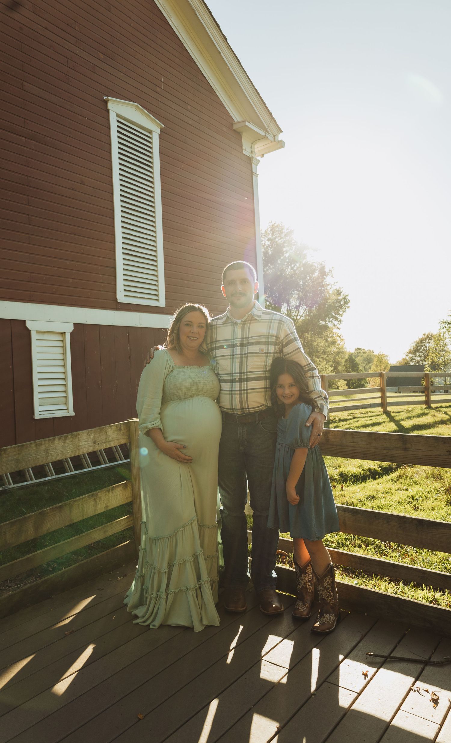 A group stands together on a wooden porch of a brown farmhouse during golden hour with sunlight casting long shadows.