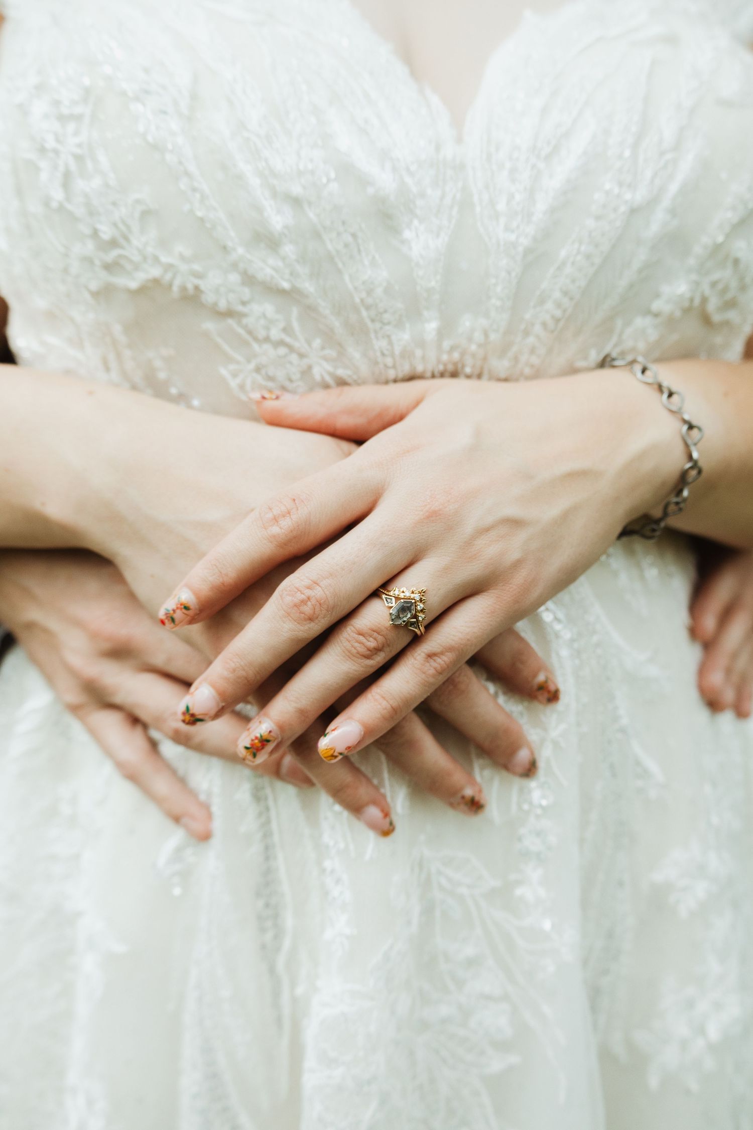 Close-up of hands showing delicate lace details on a white wedding dress and jewelry.