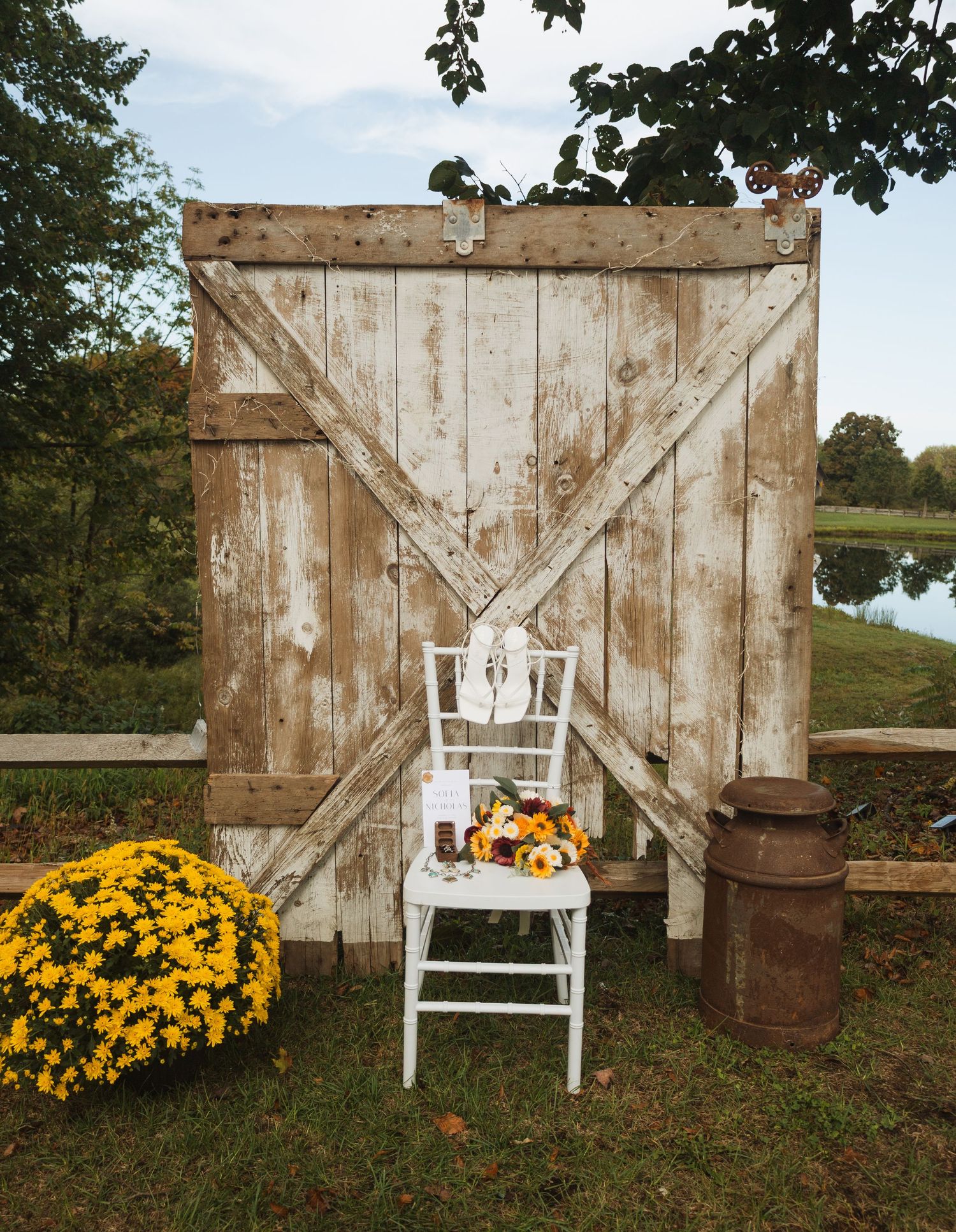 Rustic wedding decor featuring a white barn door backdrop, wooden chair, and yellow mums.