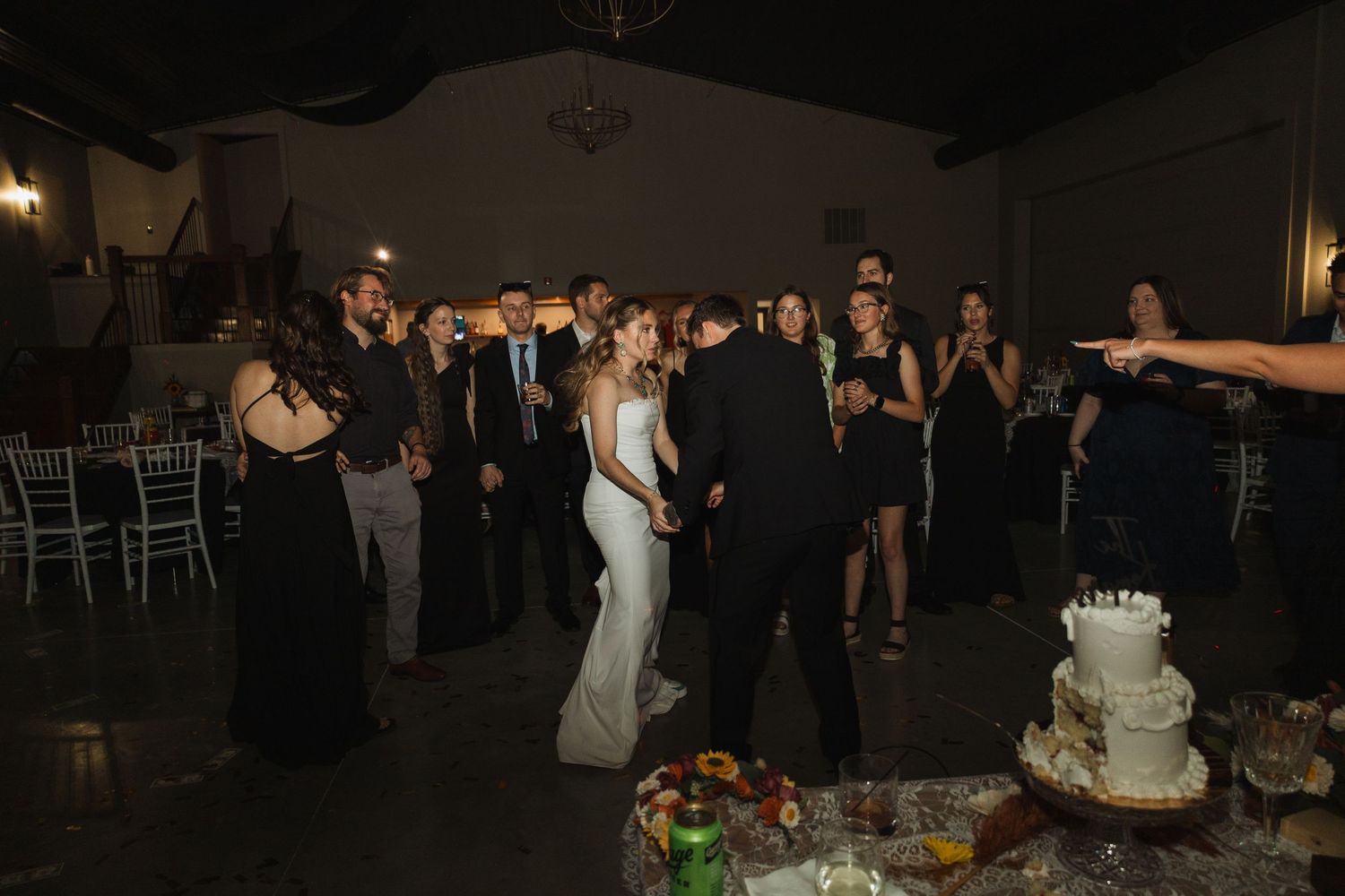 Wedding guests dancing and celebrating at a dimly lit indoor reception venue.