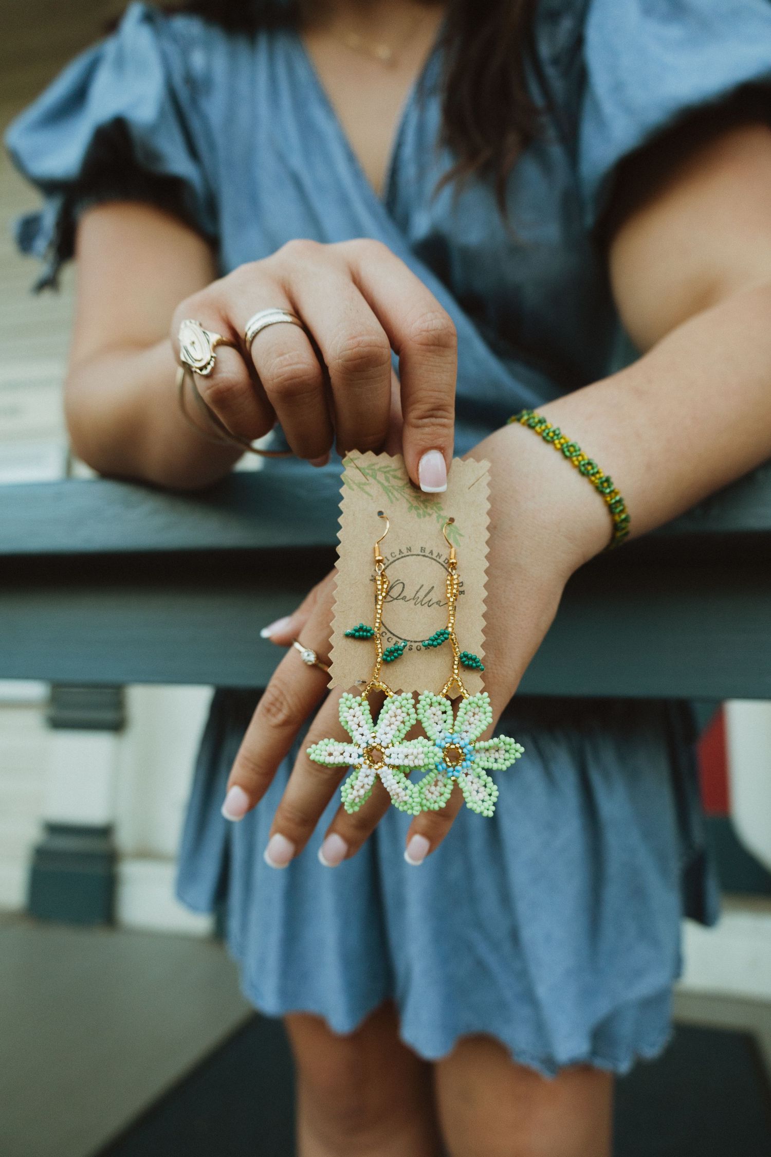 A series of five images showing hands wearing decorative butterfly and floral rings against a blue dress background.