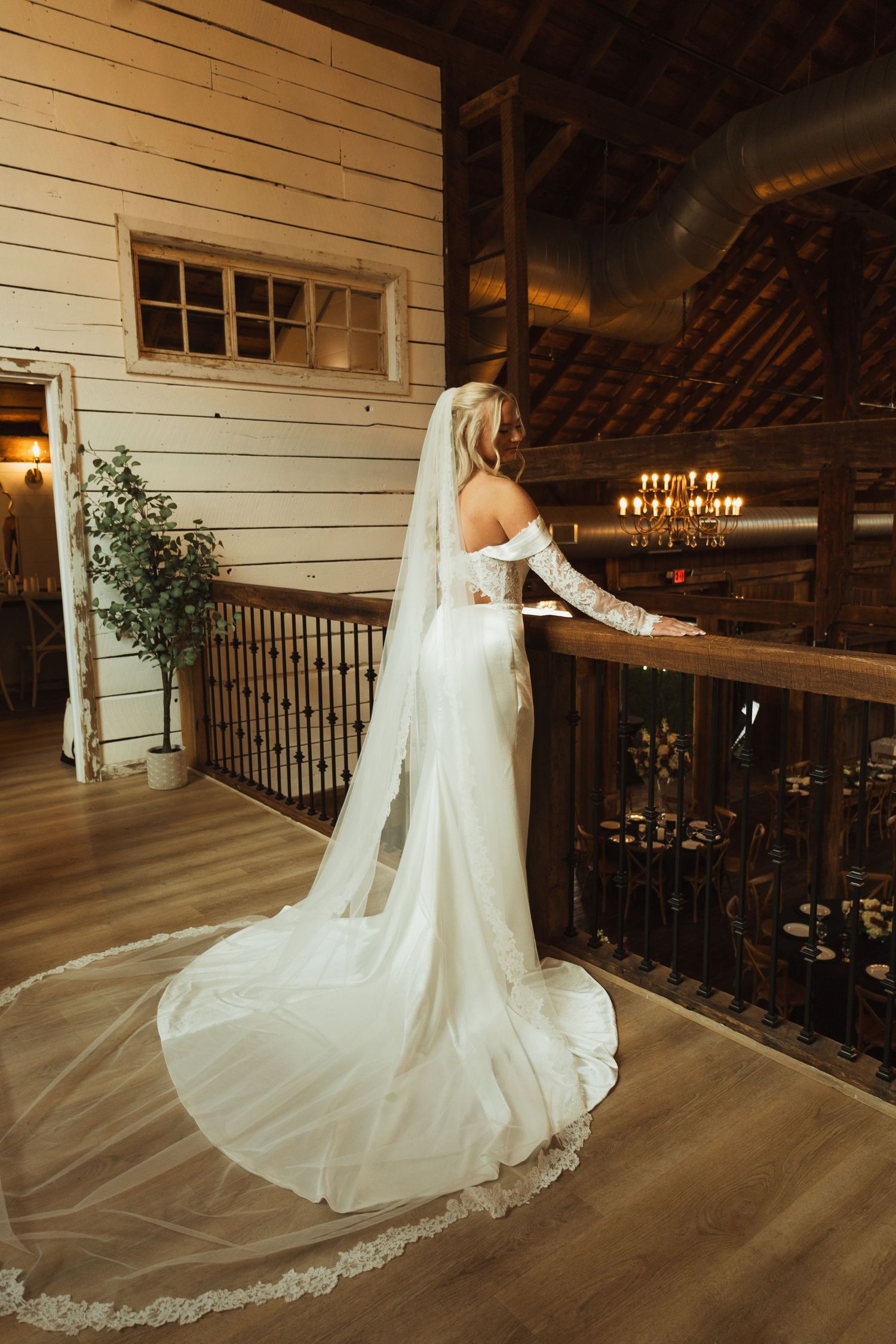 A flowing white wedding dress with long train photographed in a rustic wooden venue.