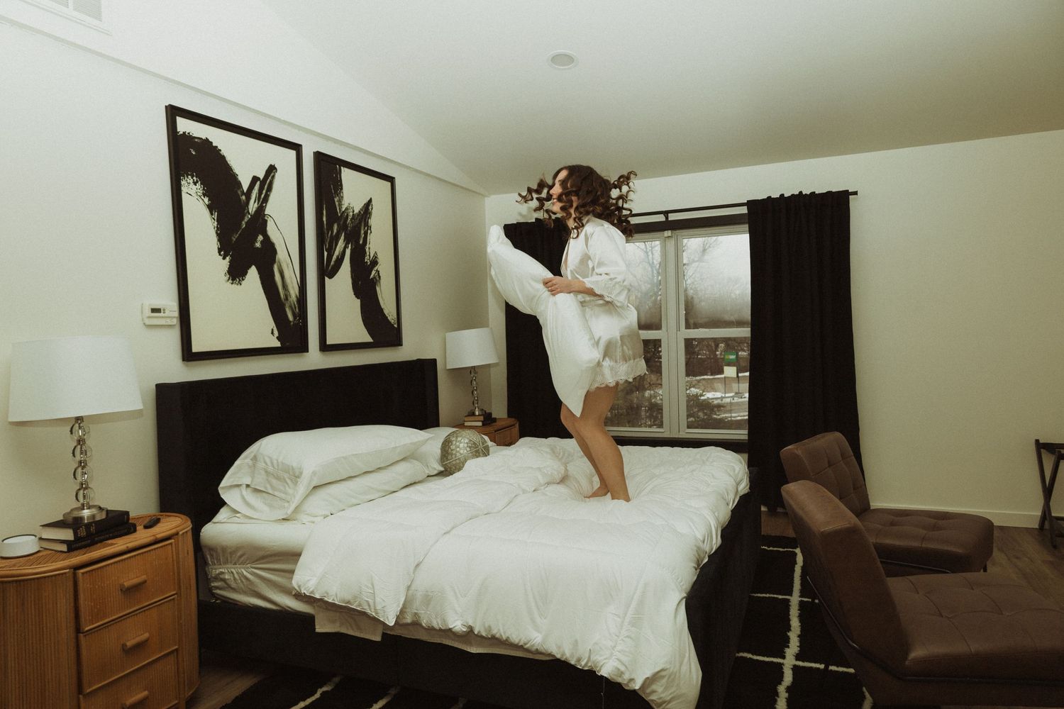 Person jumping on white bed beneath black bird artwork in modern bedroom.