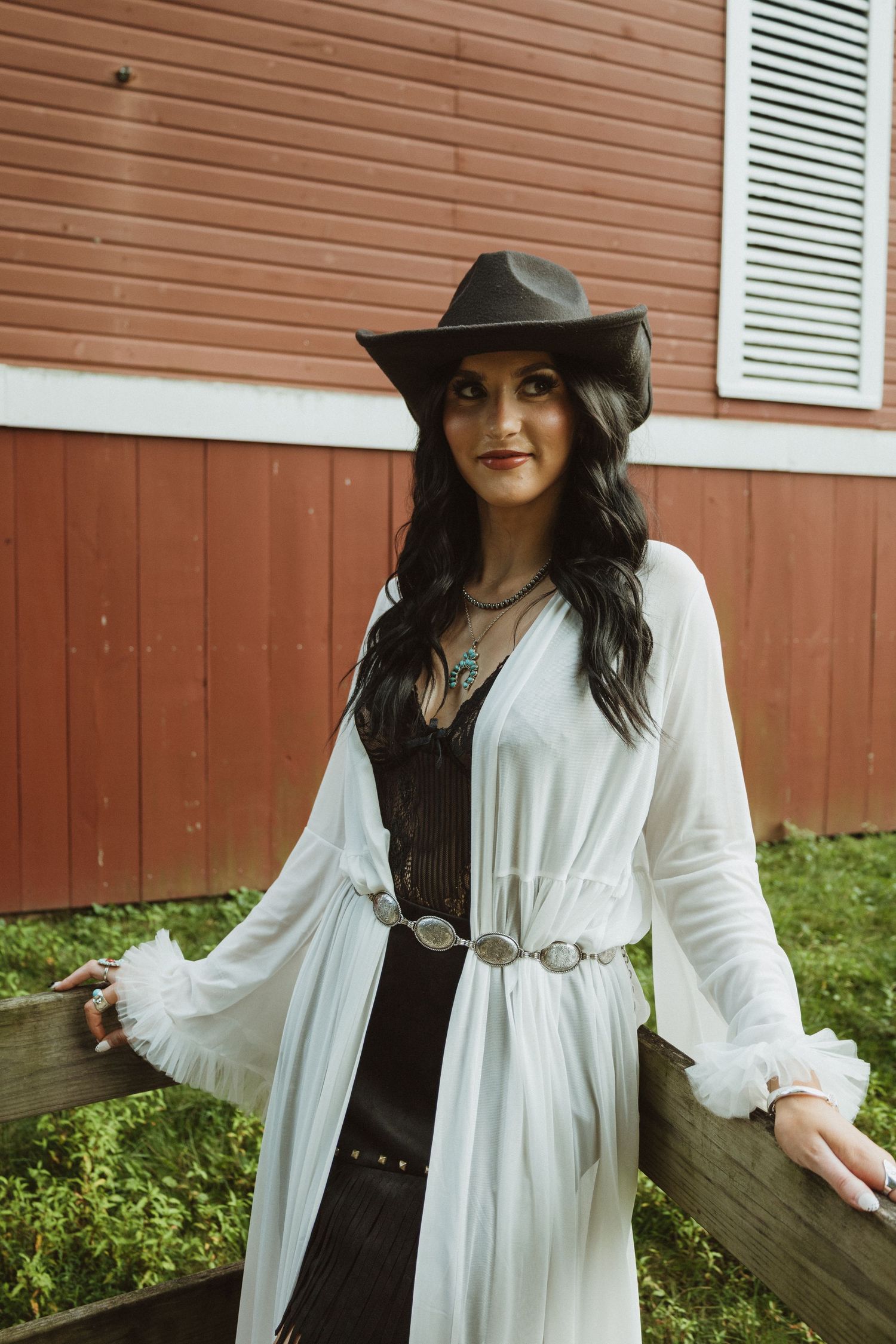 Bohemian fashion photoshoot showcasing a flowy white kimono against a rustic red barn backdrop.
