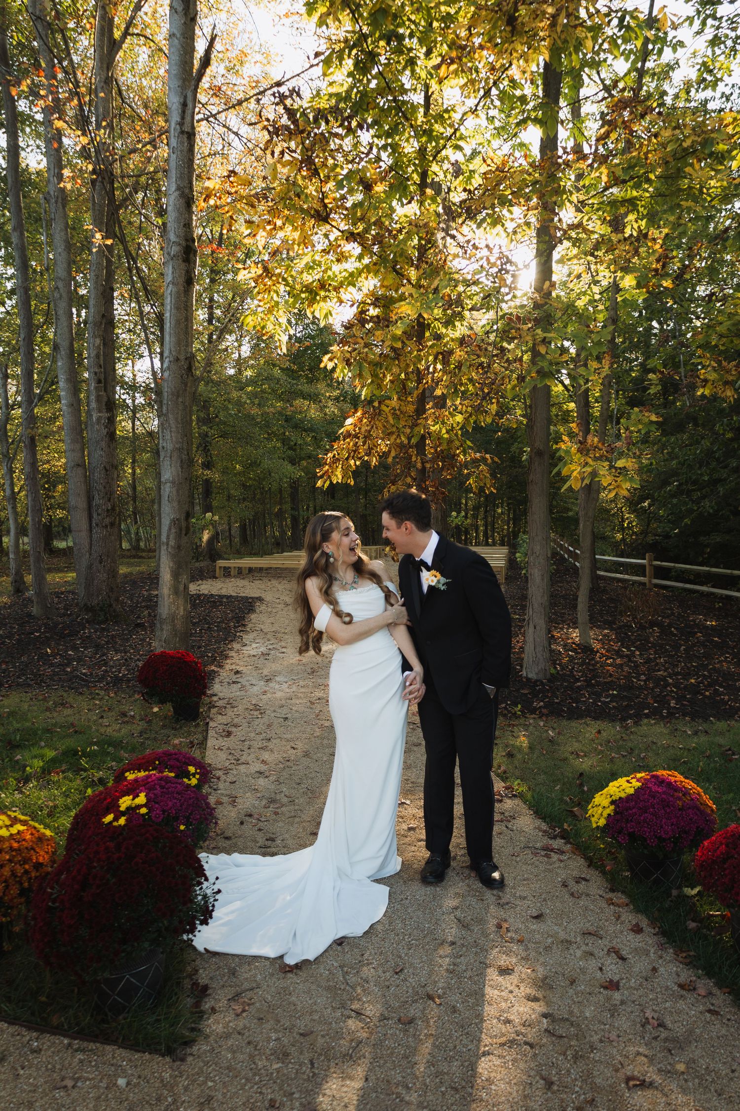A romantic autumn wedding ceremony on a tree-lined path decorated with burgundy mums and golden foliage.