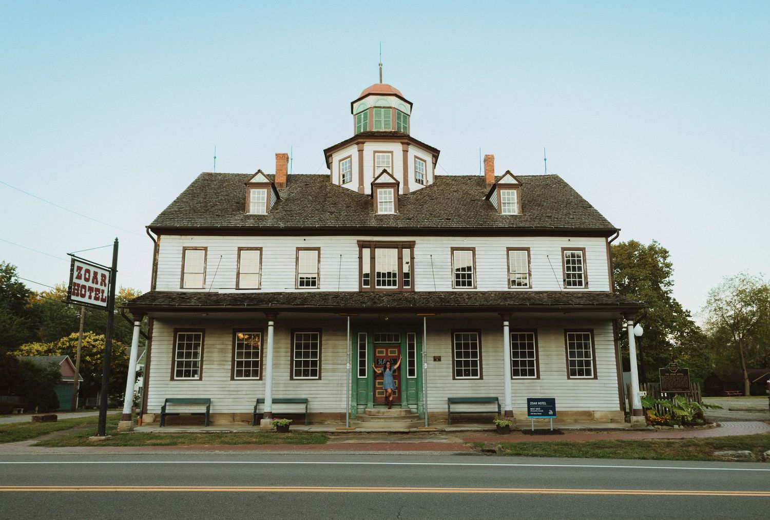 Historic colonial buildings with white siding and ornate cupola stand in a row against a bright blue sky.