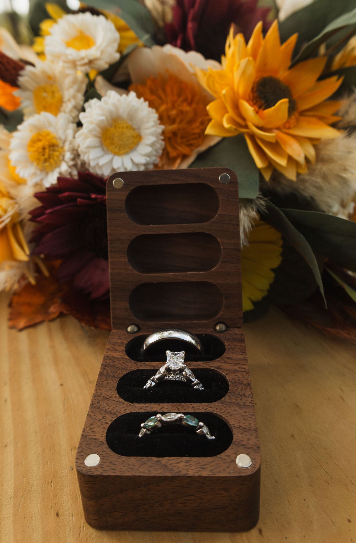 Wedding rings displayed in wooden boxes surrounded by vibrant sunflowers and daisies.