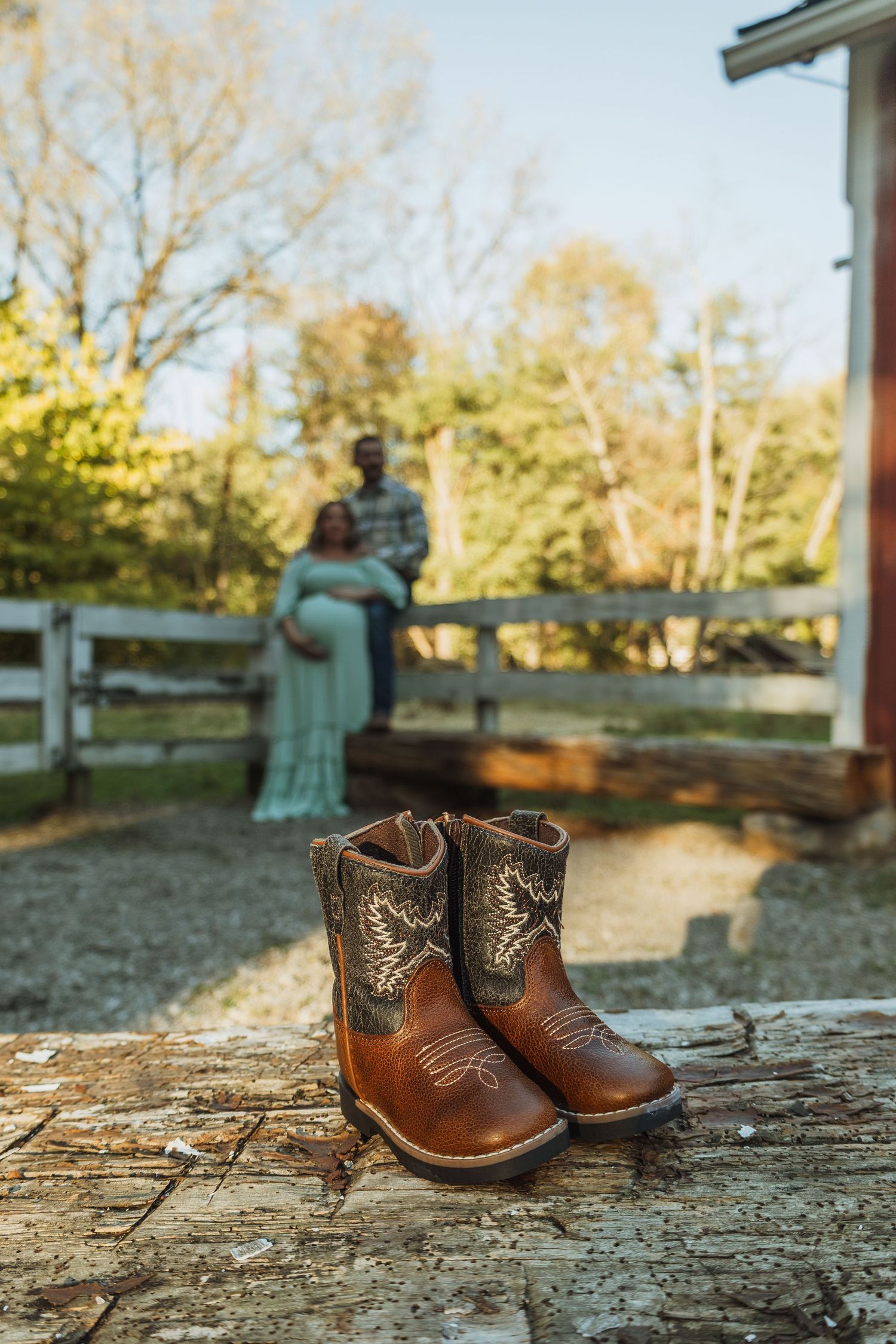 Small brown leather baby boots sit on rustic wooden surface with blurred autumn background.