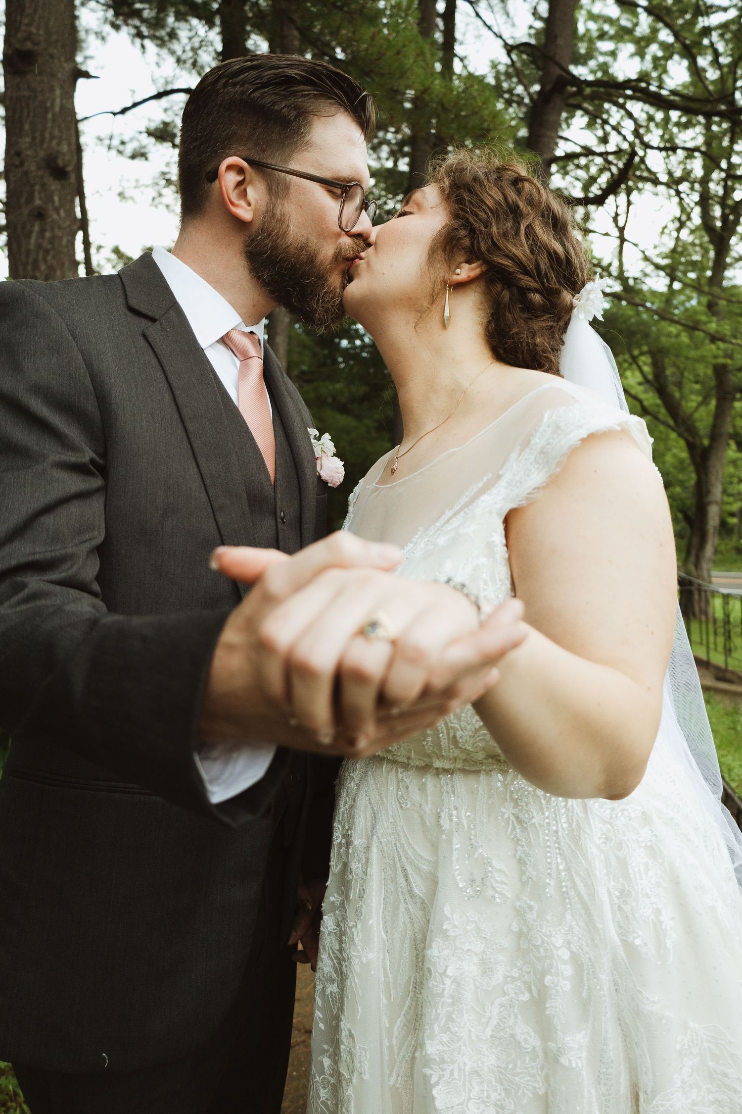 A romantic wedding couple shares a tender dance moment outdoors among trees.