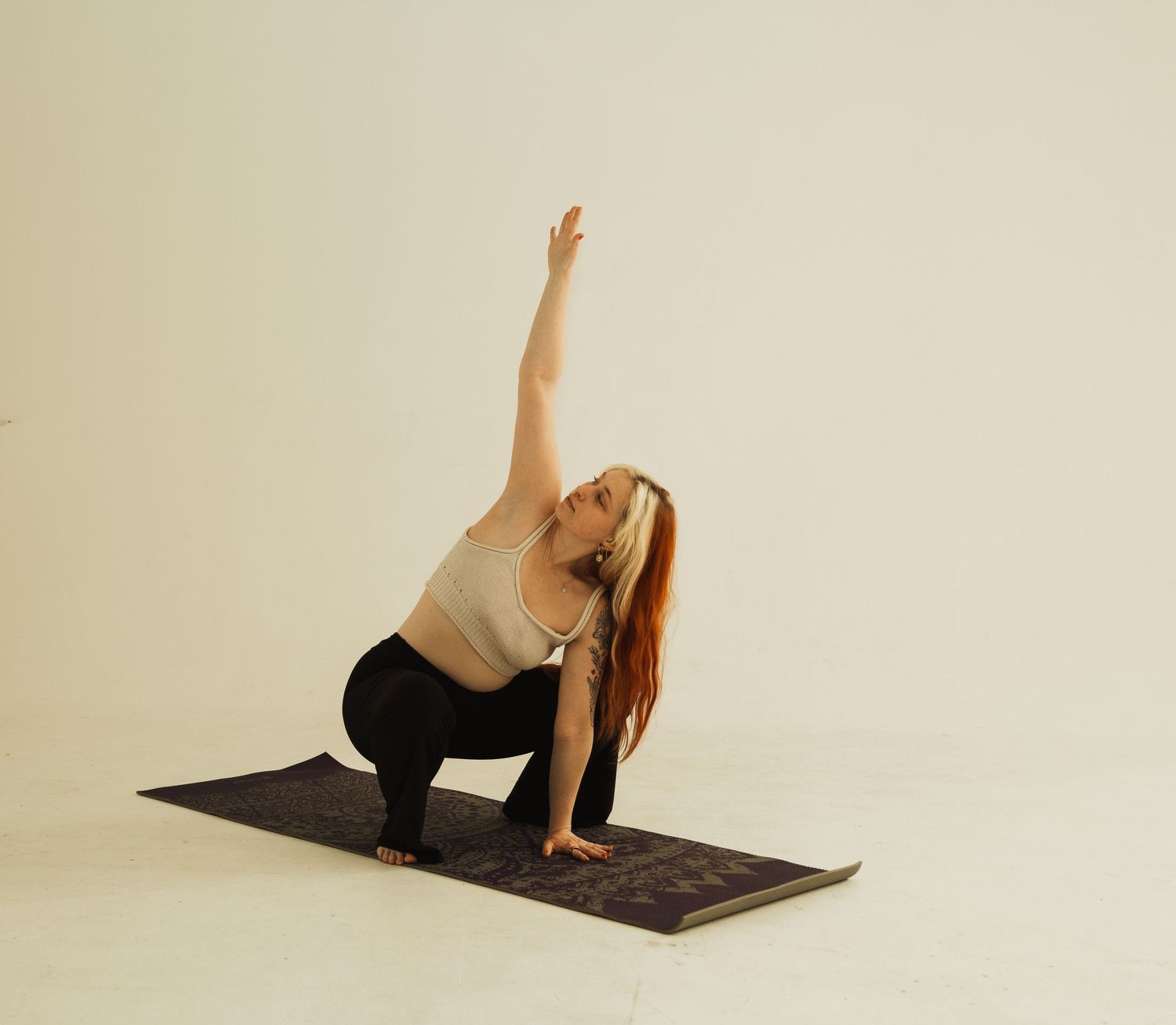 Person doing yoga on a mat in a minimalist studio setting, demonstrating side angle stretch pose in white attire.
