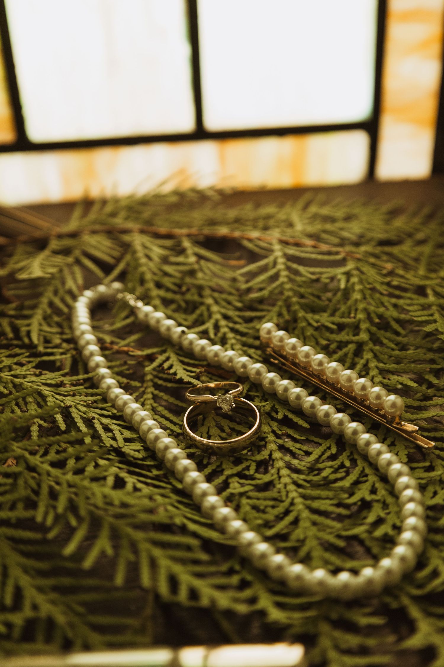 Pearl necklace, ring, and hair pin arranged on green pine branches for a winter wedding flat lay.