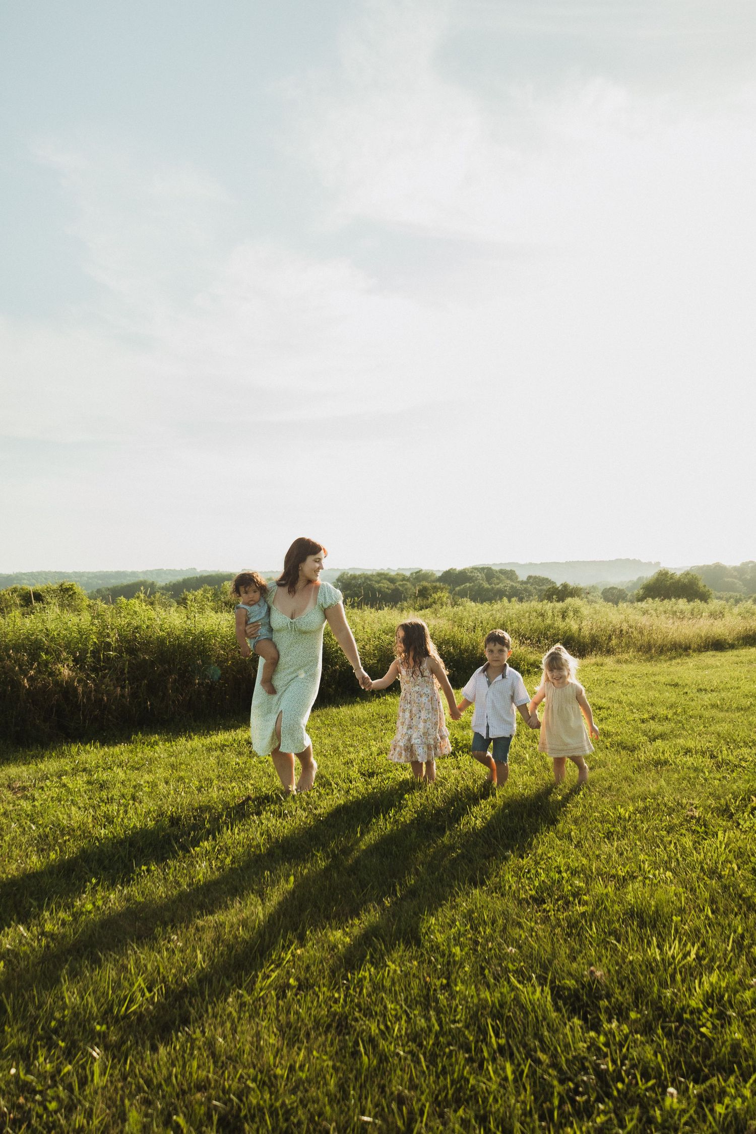 Family silhouettes walking together across a hilltop meadow during sunset.