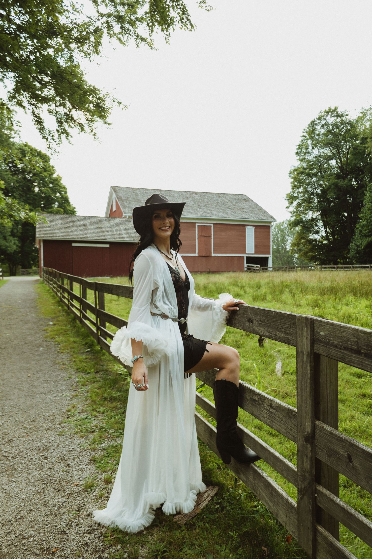 A flowing white dress creates an ethereal mood against a rural farm setting with wooden fences and green fields.