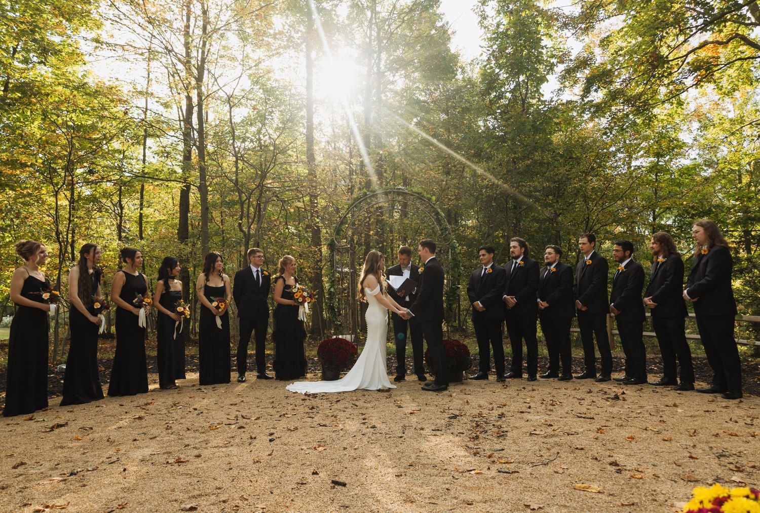 Wedding party lined up along a tree-lined path during golden hour with autumn foliage.