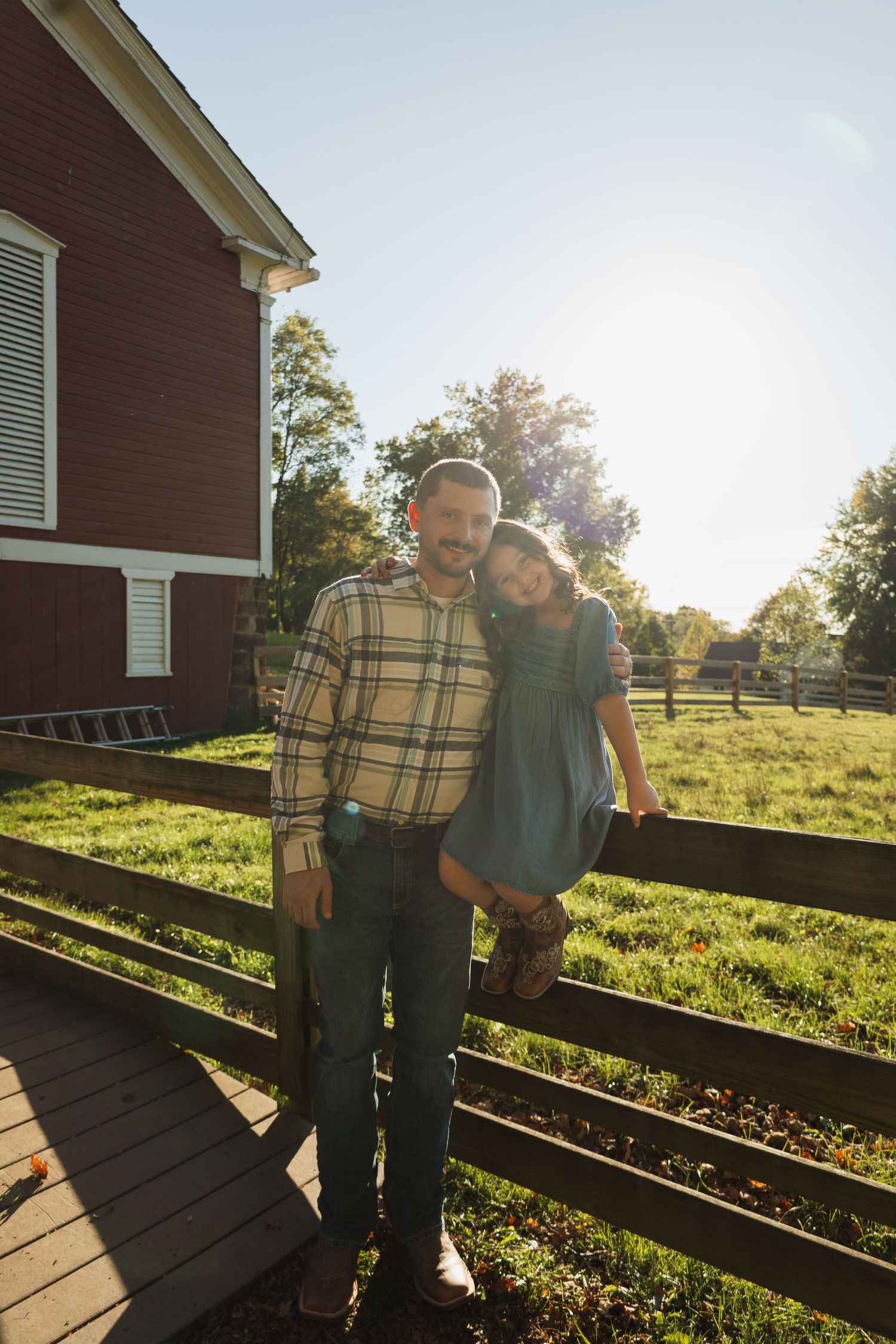 Two people stand together on a wooden deck outside a red barn on a sunny autumn afternoon.
