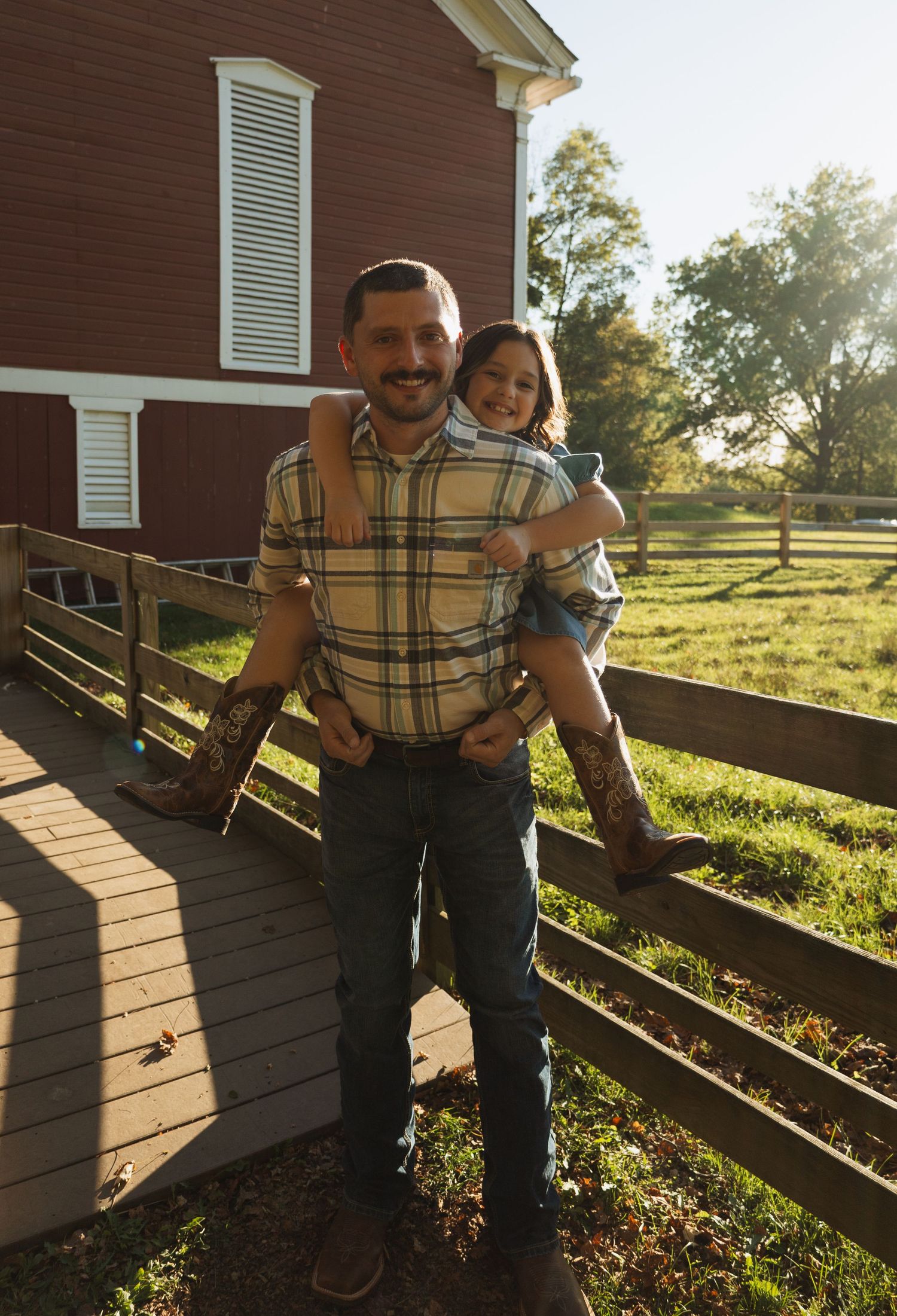 A couple sits together on a wooden deck railing during golden hour at a rustic farmhouse.
