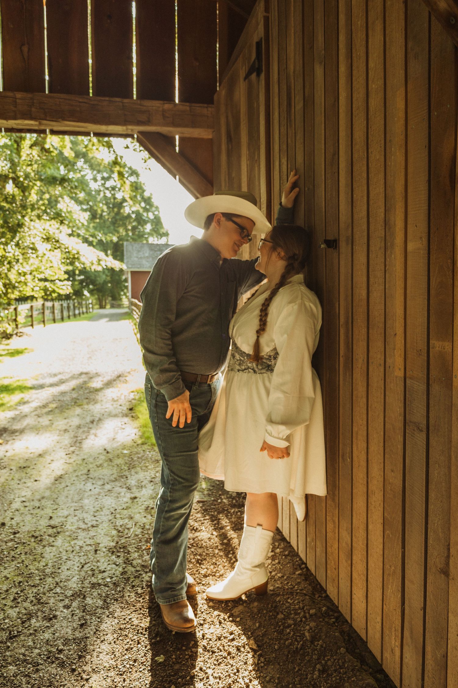 Romantic couple embracing against a rustic wooden barn wall on a sunny afternoon.